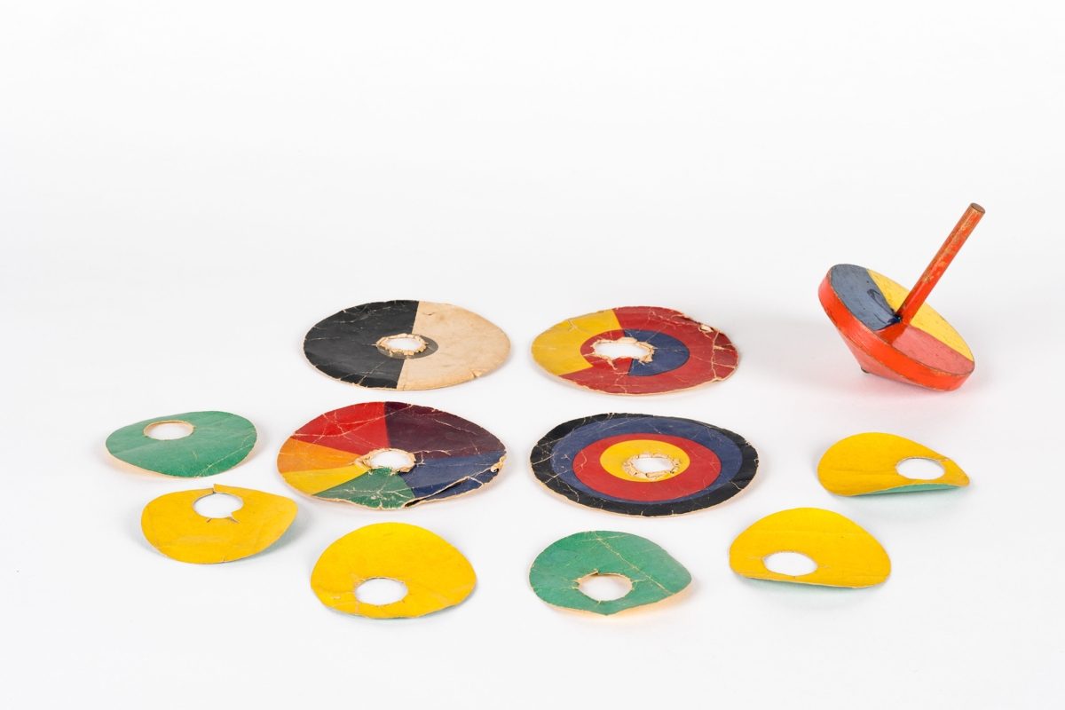 Bunte Holzspielzeuge: ein Kreisel und mehrere flache, farbige Scheiben auf einem weißen Hintergrund.