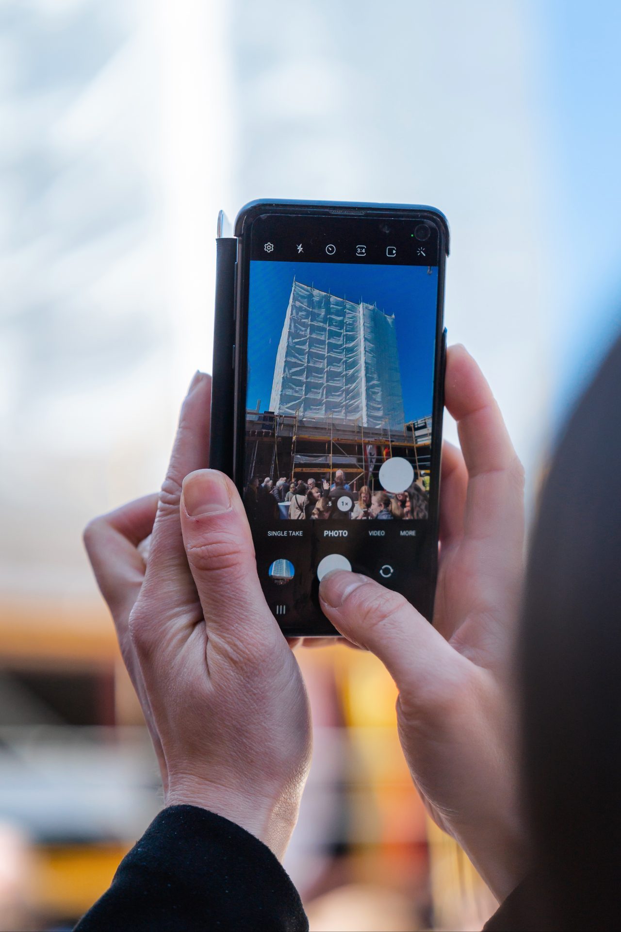 Eine Person hält ein Smartphone und fotografiert ein modernes Gebäude im Freien.