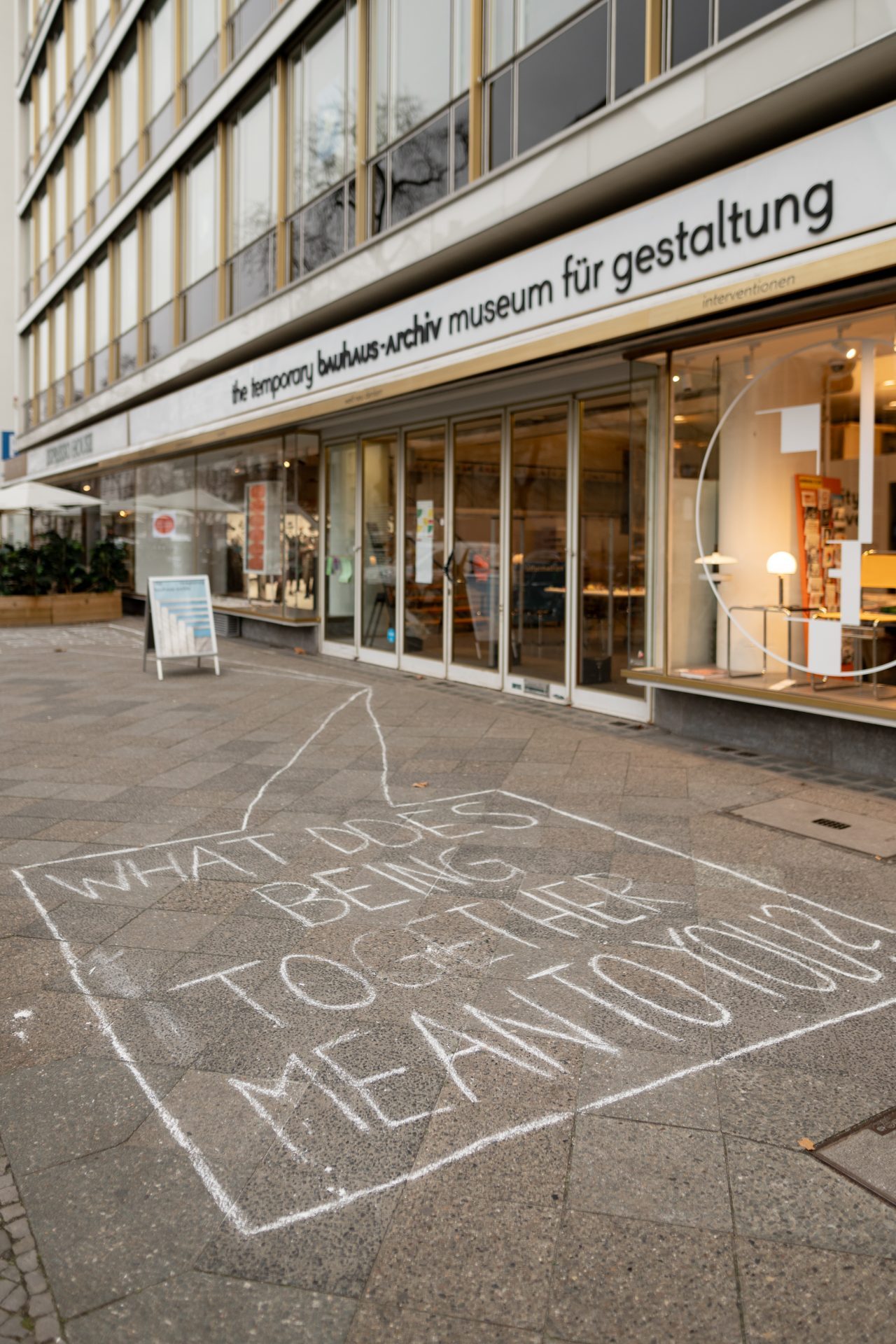 Graffiti auf dem Bürgersteig vor einem Museum mit der Frage: "Was bedeutet es, hier zu sein?"