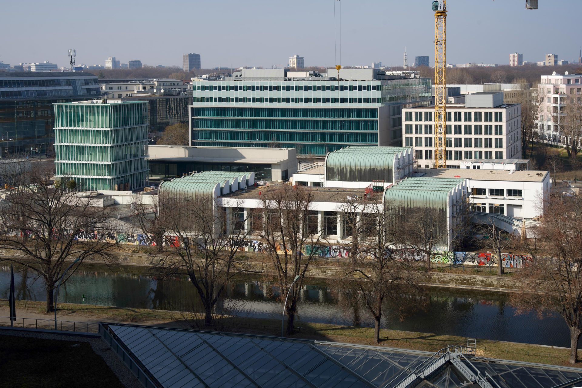 Foto des Bauhaus-Archivs mit Neubau am Landwehrkanal, mit Bäumen im Vordergrund und einem gelben Kran im Hintergrund.