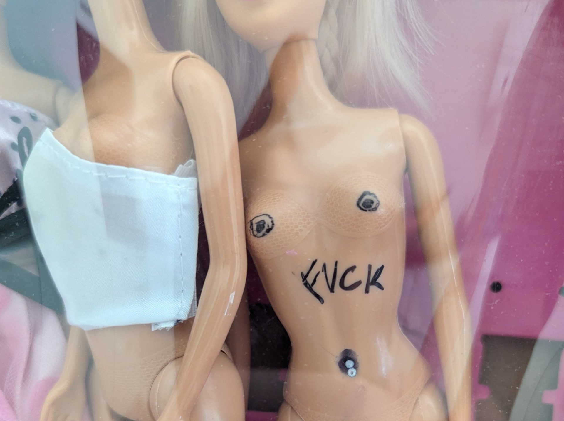 Foto von zwei Barbiepuppen in einem Display, eine trägt ein weißen Oberteil, die andere hat den schwarzen Schriftzug "Fuck" auf dem Bauch.