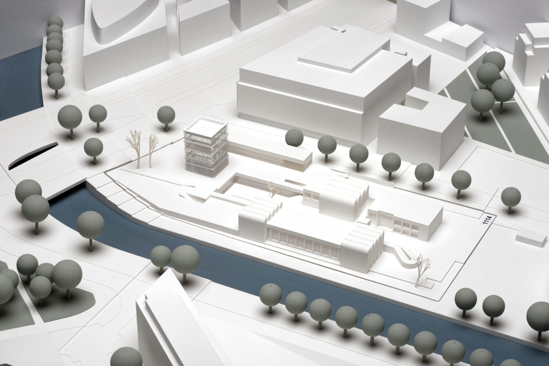 Architekturmodell mit weißen Gebäuden, Bäumen und einem Fluss in minimalistischer Gestaltung.