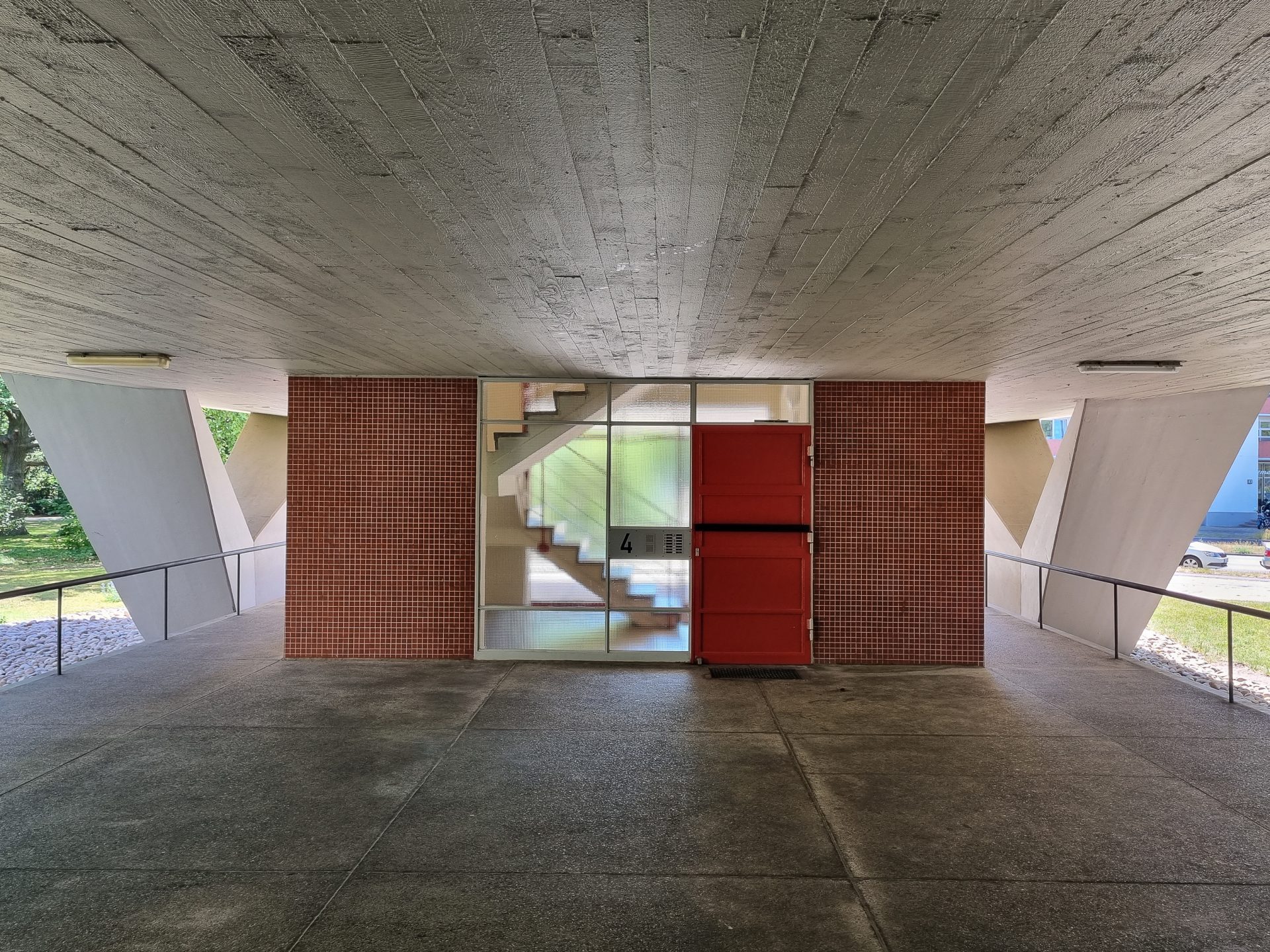 Modern architecture featuring concrete walls, a glass façade, and a red staircase in an open space.