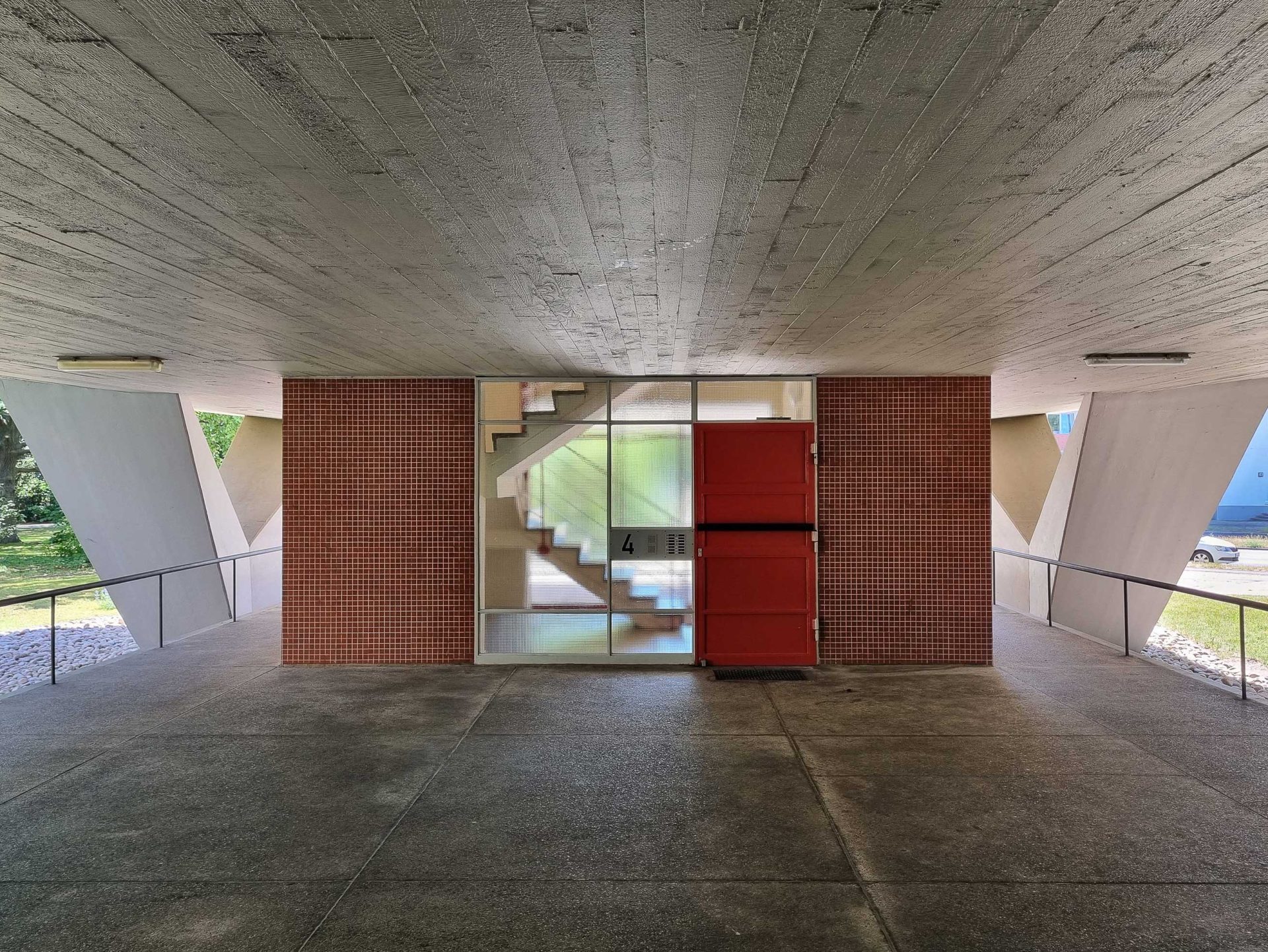 Moderne Architektur mit Betonwänden, Glasfront und roter Treppe in einem offenen Raum.