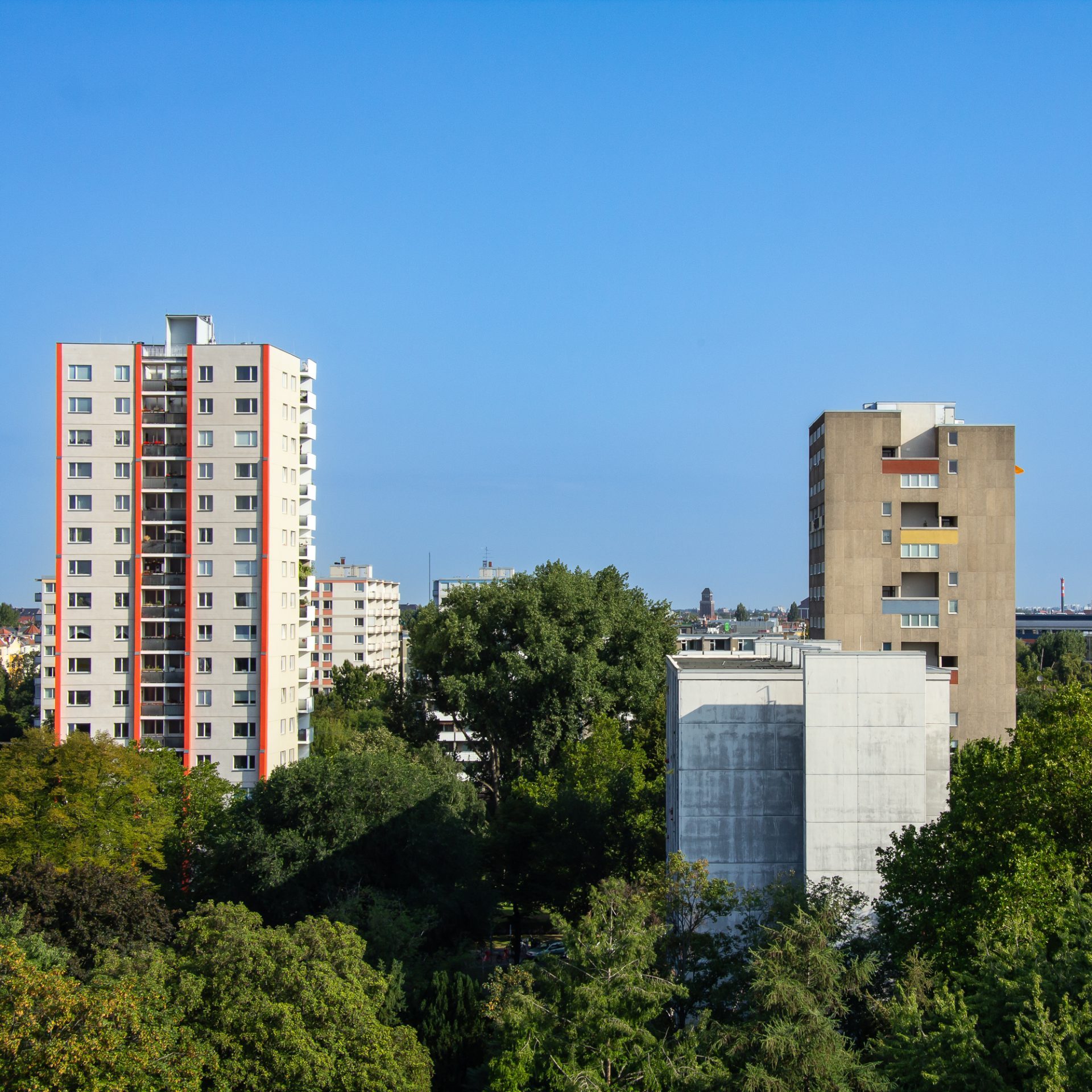 Städtische Architektur mit Hochhäusern, umgeben von Bäumen und blauem Himmel.