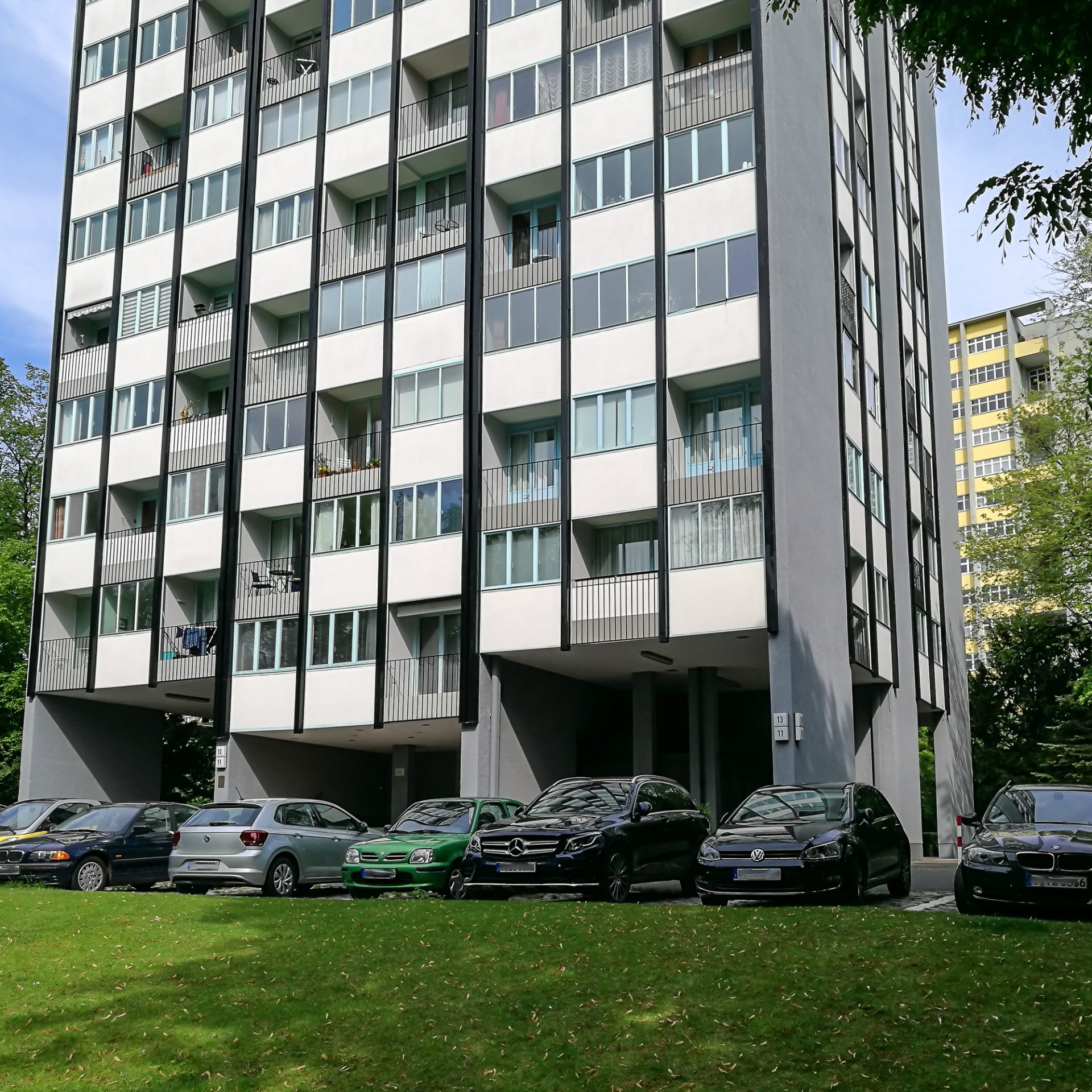 Moderne mehrstöckige Wohnhäuser mit parkenden Autos auf einer Rasenfläche im Vordergrund.