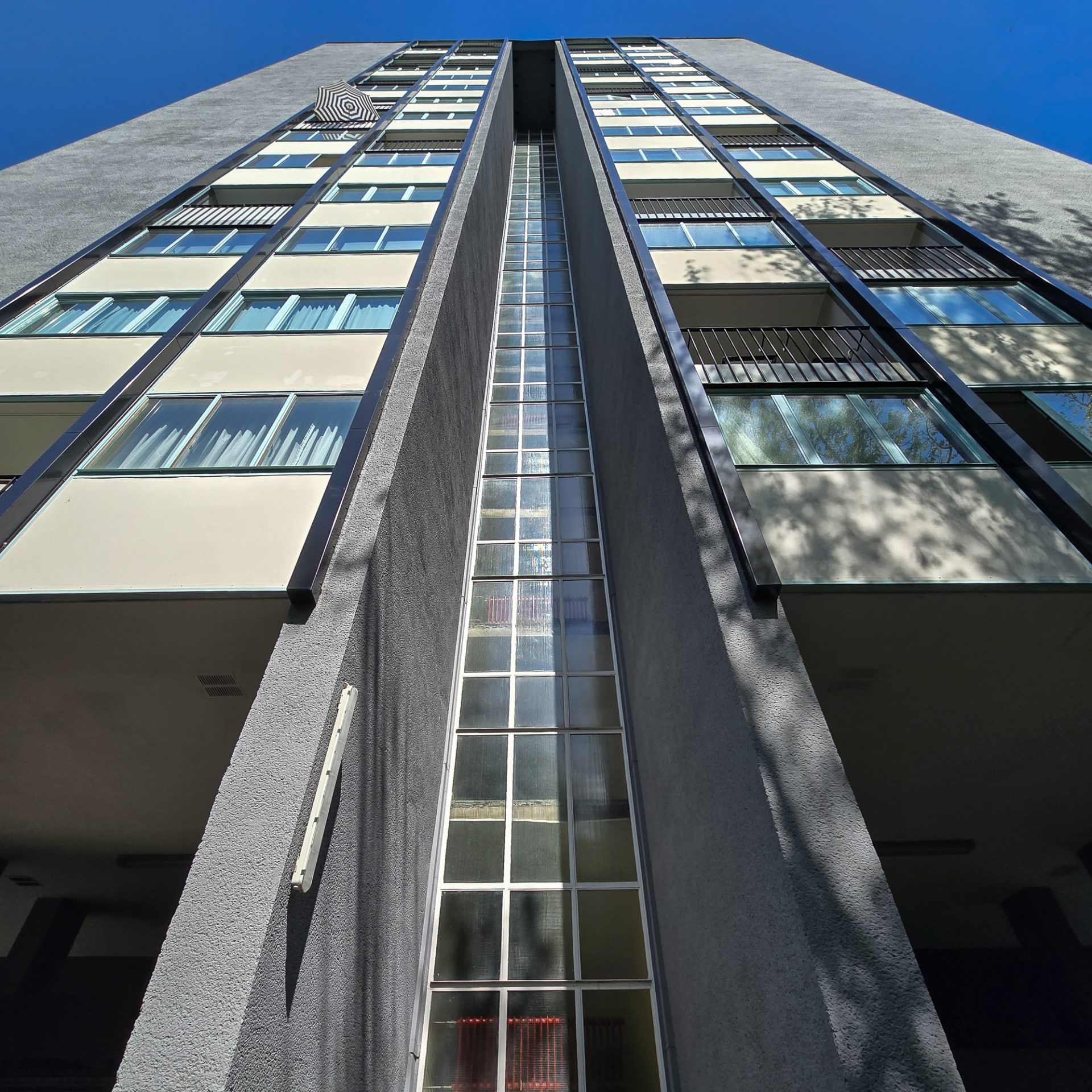 Blick nach oben auf ein modernes Wohngebäude mit großen Fenstern und klaren Linien unter einem blauen Himmel.