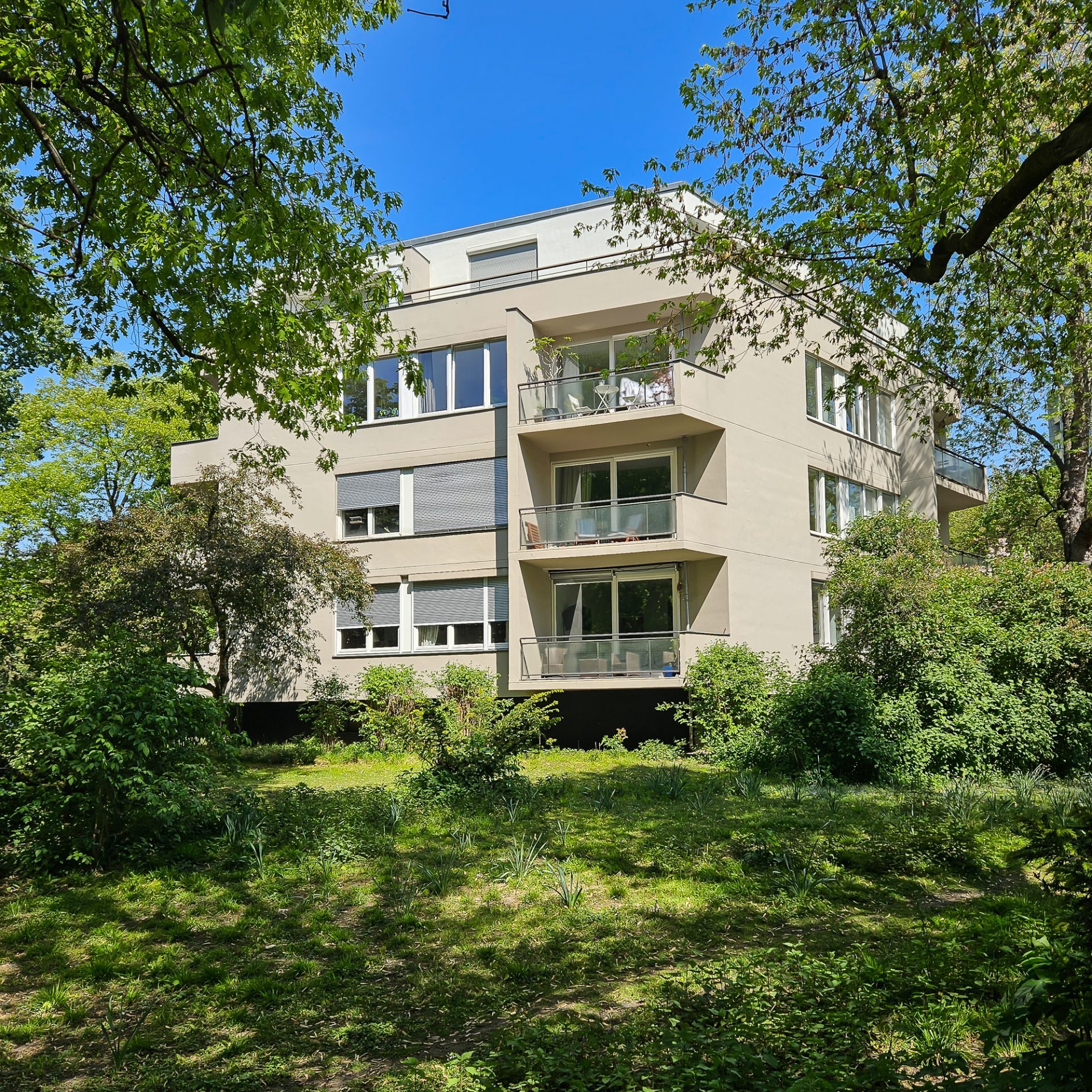 Moderne Wohngebäude, umgeben von Bäumen und Grünflächen, unter einem klaren blauen Himmel.