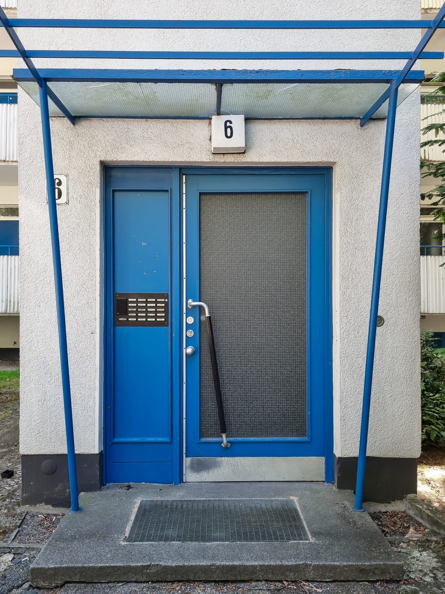 Blaue Eingangstür mit Vordach, Hausnummer 6, Gegensprechanlage und mattem Fenster.