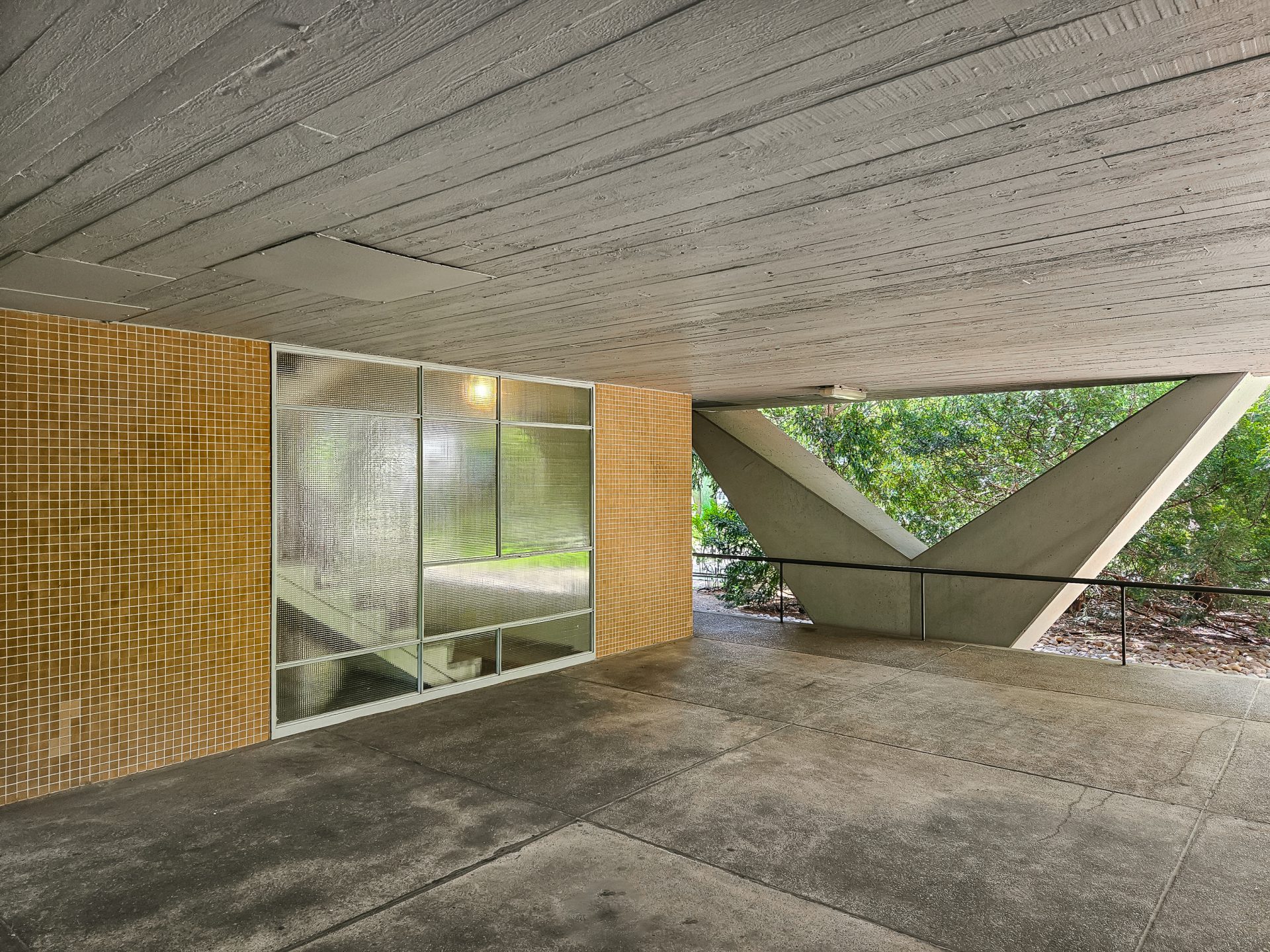 Moderne Architektur mit Sichtbeton, großen Fenstern und einem offenbaren, strukturierten Raum, eingebettet in Grün.