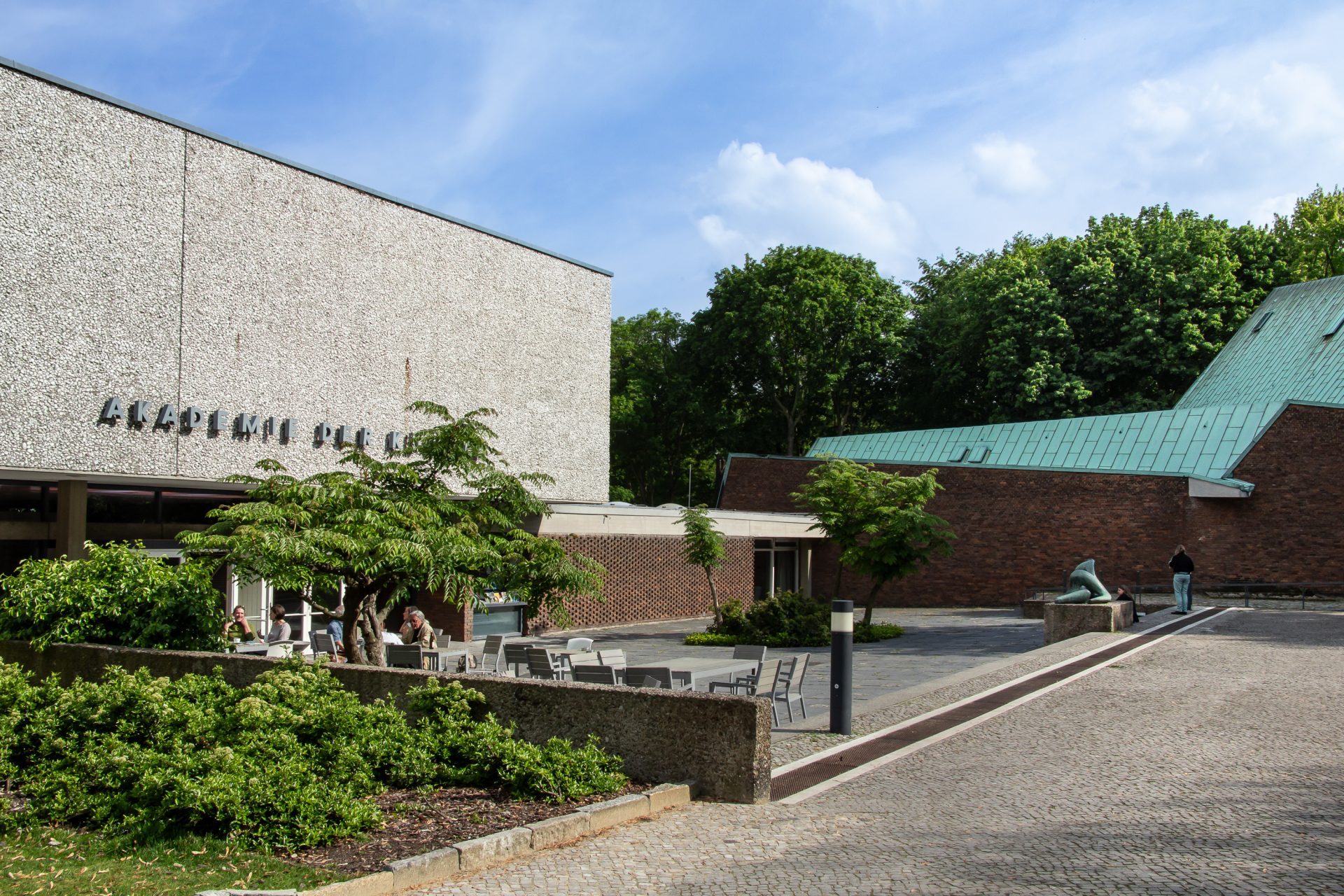 Modernes Gebäude mit klaren Linien, umgeben von Grün an einem sonnigen Tag.