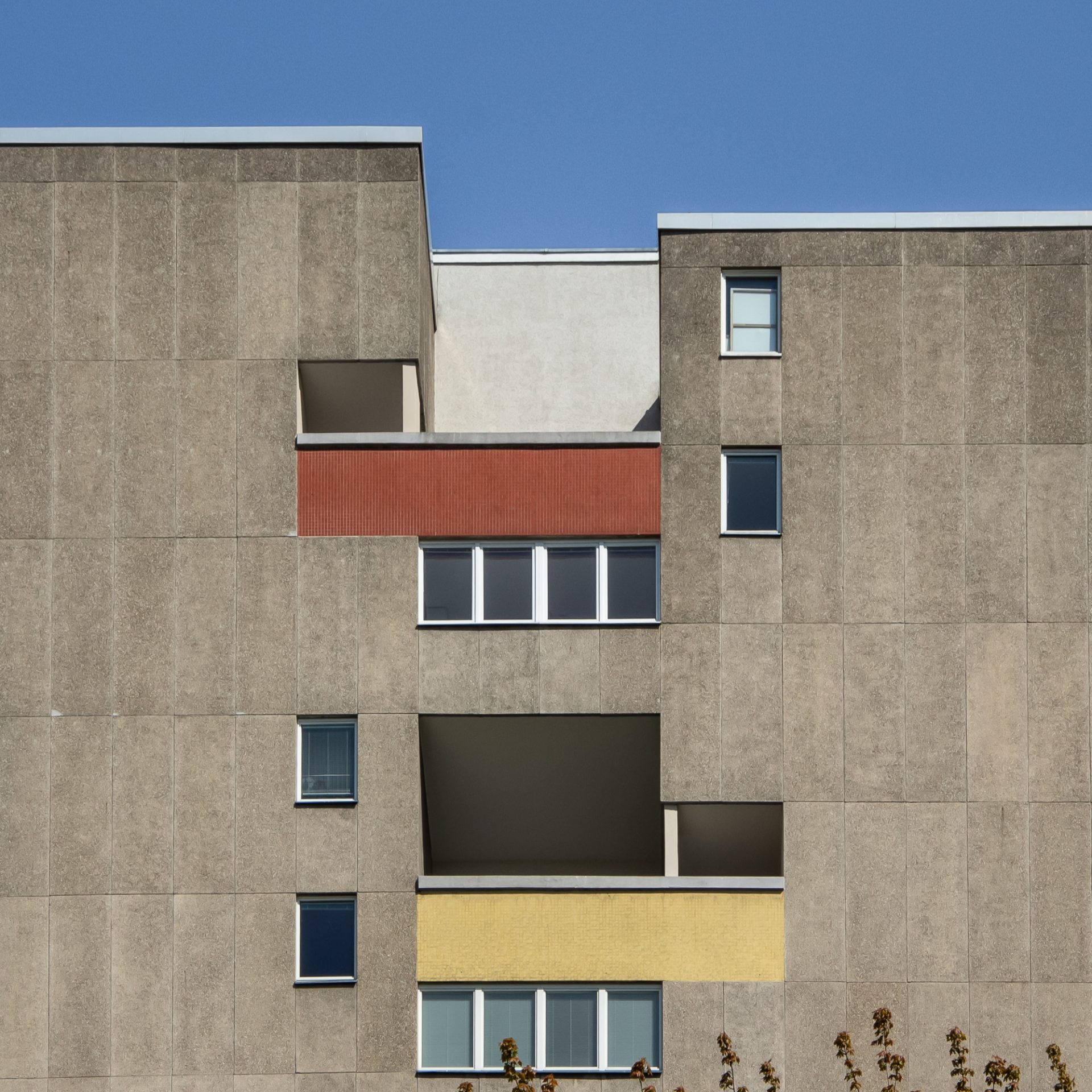 Moderne Architektur mit geometrischen Fassadenelementen in Grau, Rot und Gelb vor strahlend blauem Himmel.
