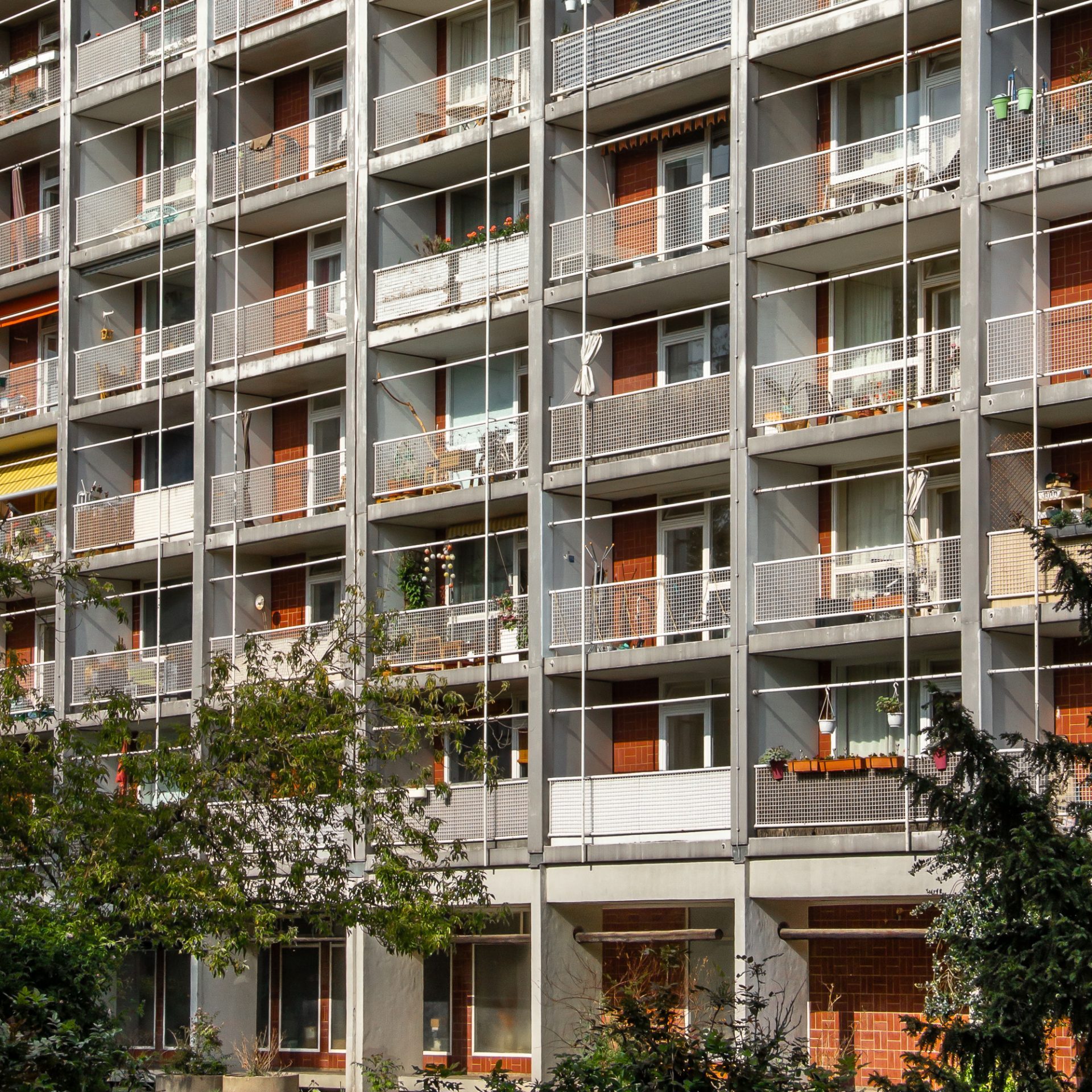 Hochhausfassade mit Balkonen und Pflanzen, moderne Wohnarchitektur in städtischer Umgebung.