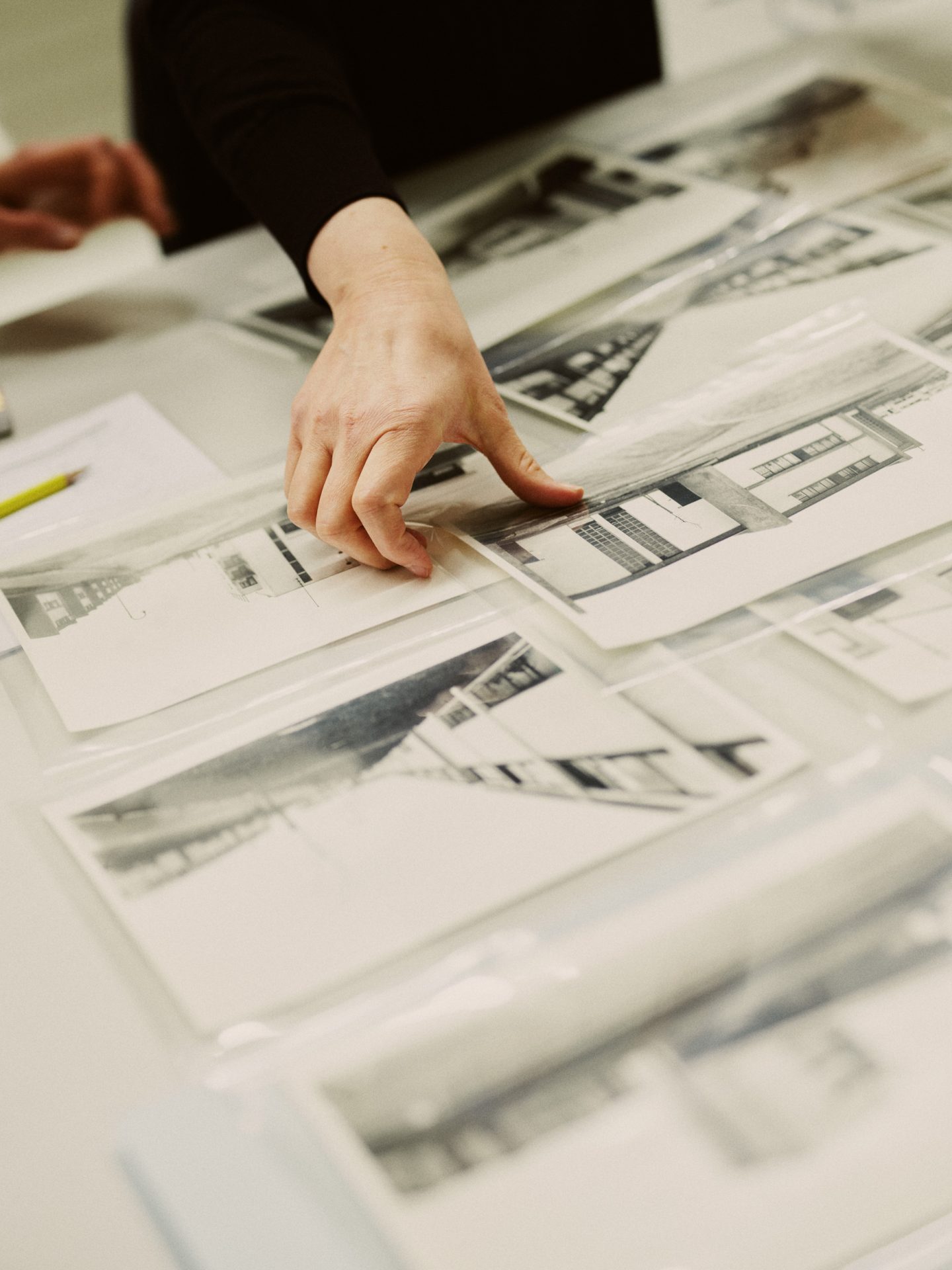 A hand examines black-and-white photographs lying in sleeves on a table.