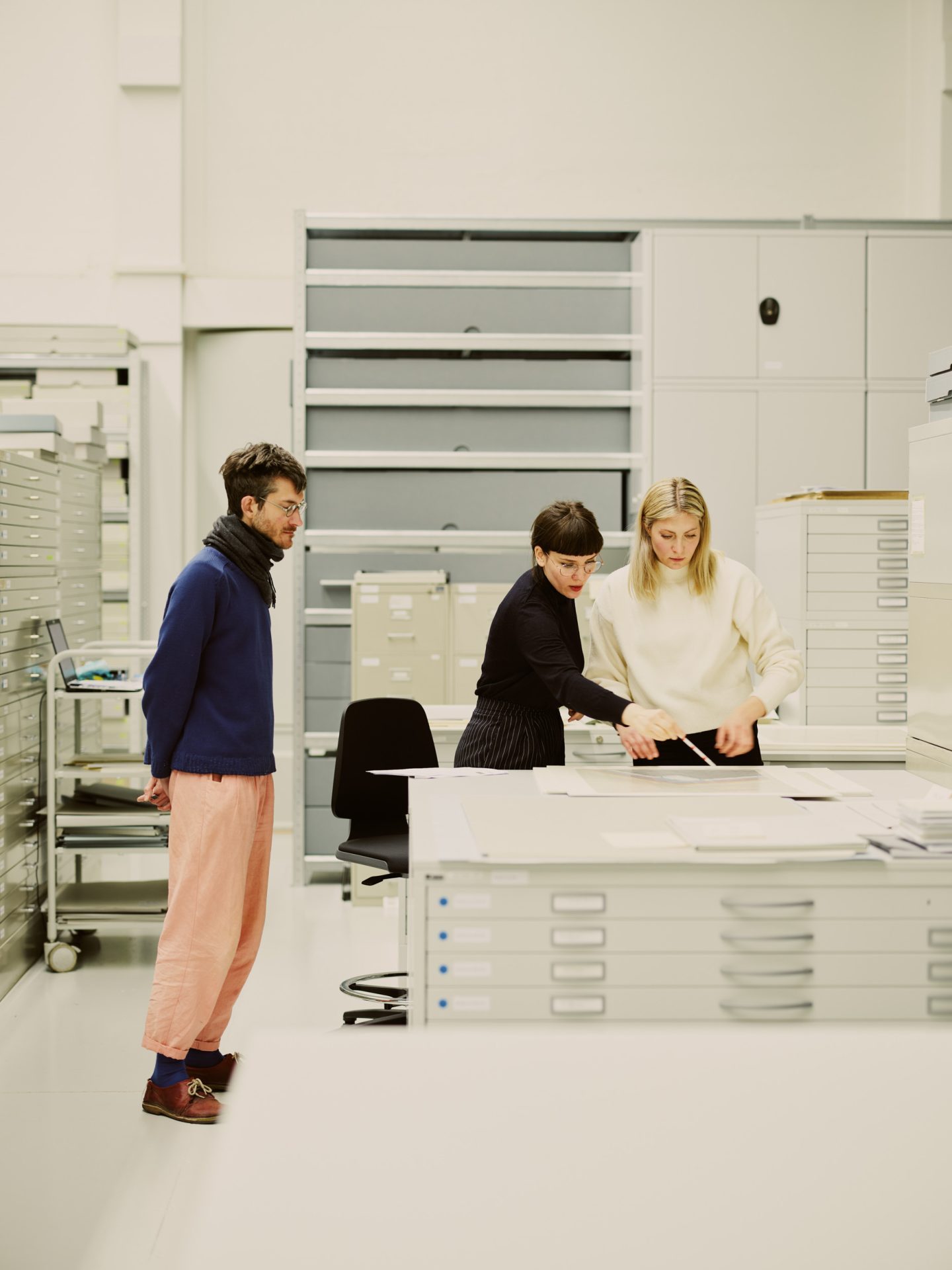 Three people are standing in a modern room, working at a table with documents.