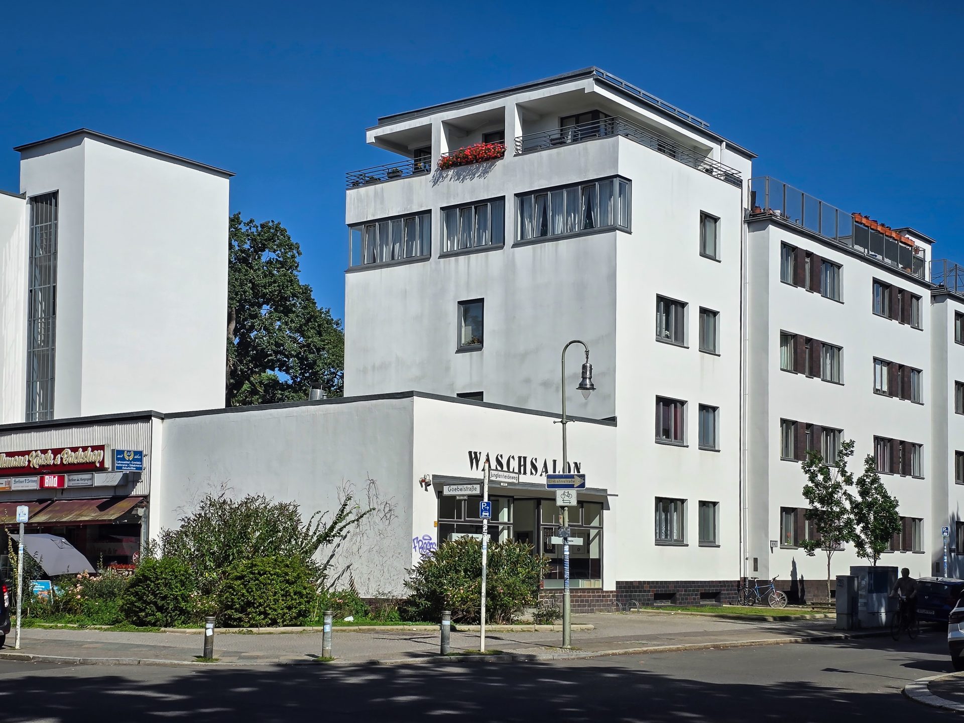 Modernes Gebäude mit klaren Linien, einer Waschsalon-Werbung und umgebenden Bäumen unter blauem Himmel.