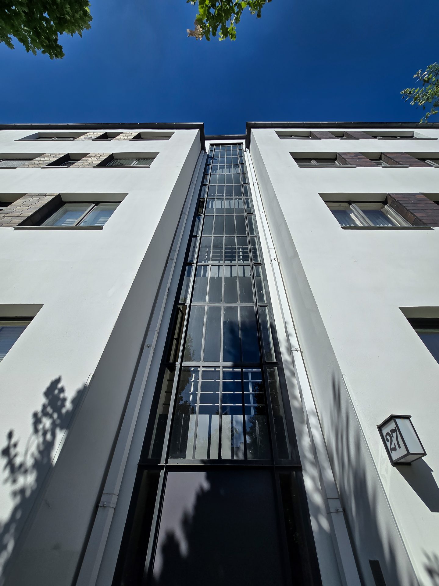 Blick nach oben auf ein modernes, weißes Gebäude mit großzügigen Fenstern und einer Glasfassade.