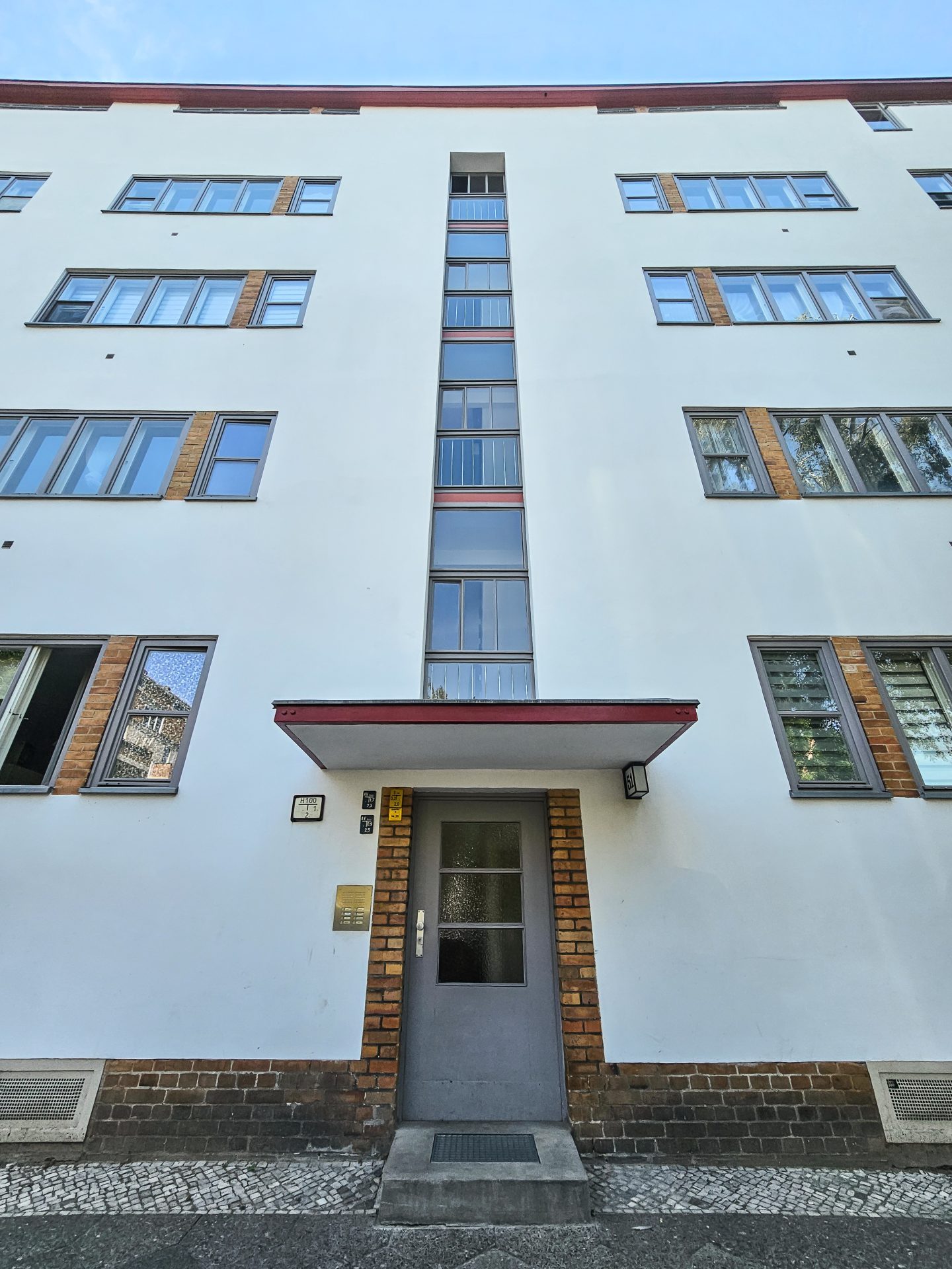 Moderne, weiße Wohnhausfassade mit großen Fenstern und zentralem Eingang. Urbaner Architekturstil.