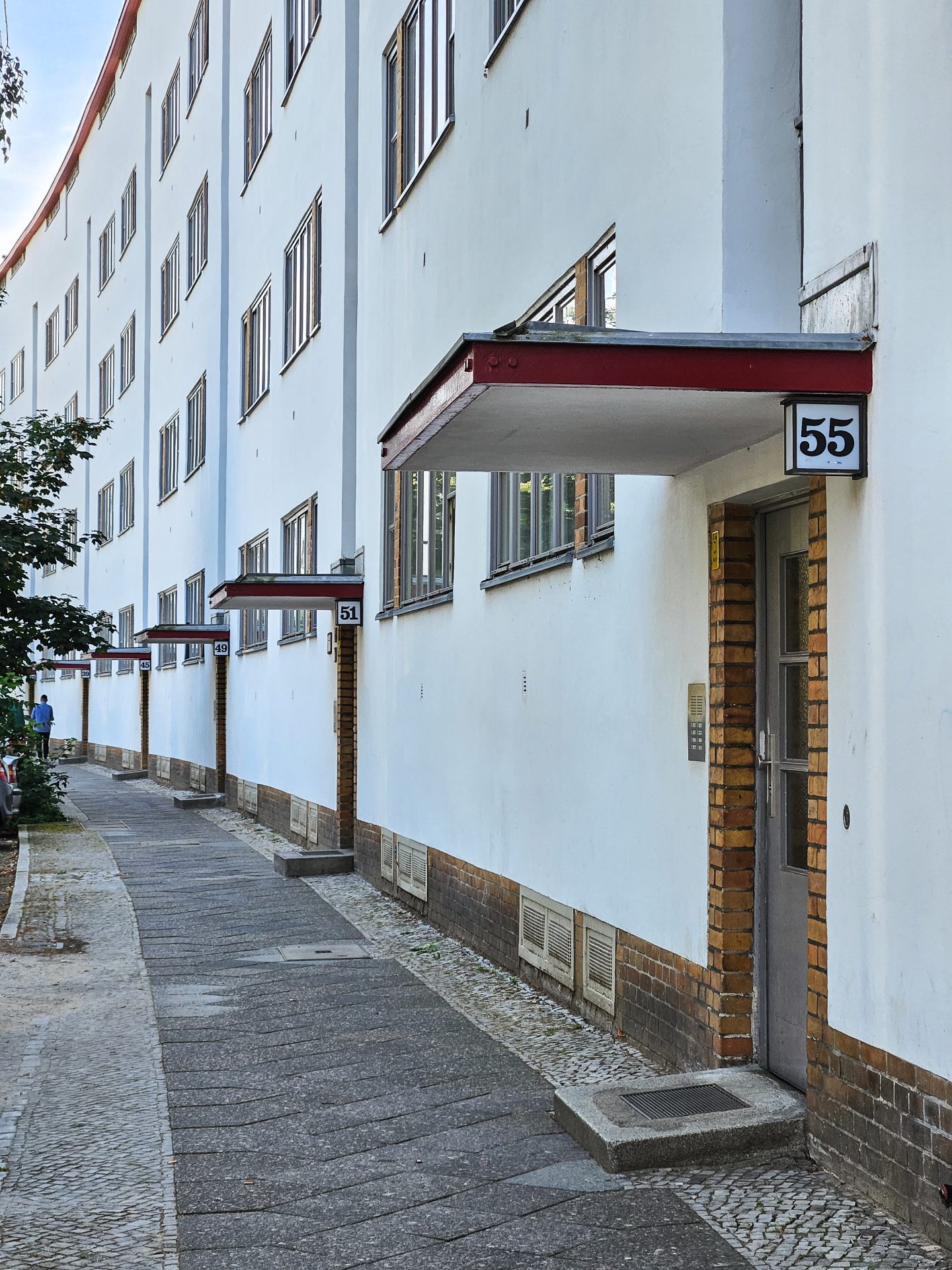 Blick auf eine moderne Wohnanlage mit weißen Wänden und Eingängen, gekennzeichnet durch die Hausnummer 55.