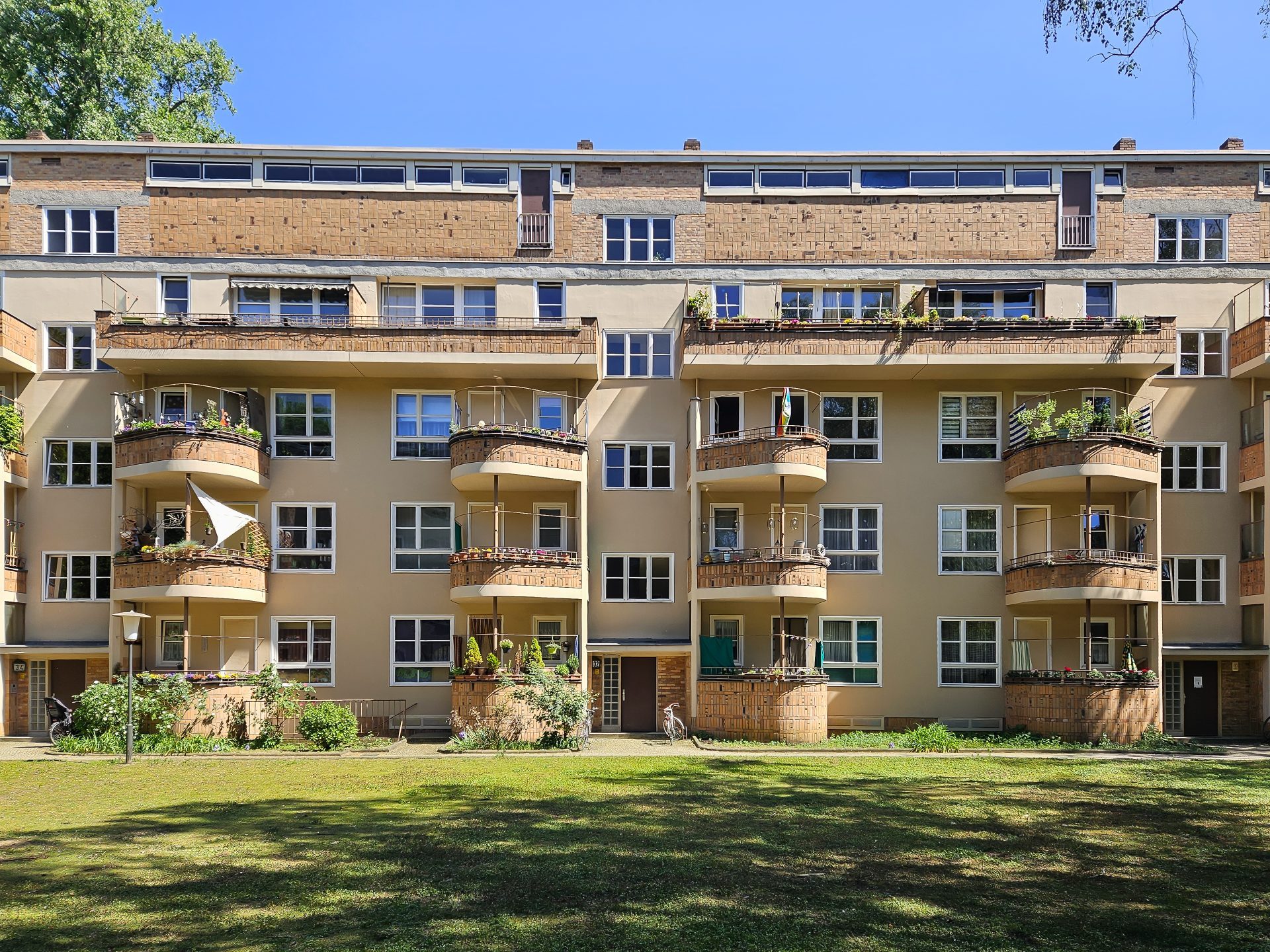 Mehrstöckiges Wohnhaus mit Balkonen und grünem Vorgarten unter blauem Himmel.