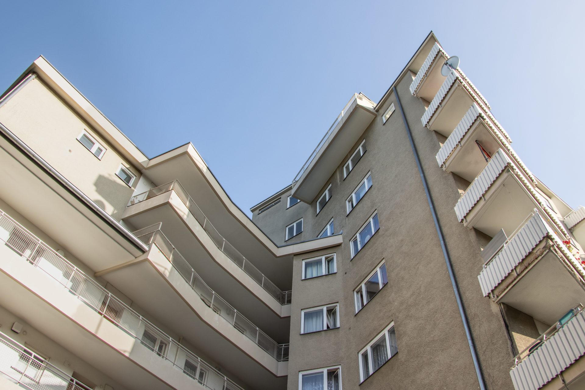Moderne Wohnanlage mit geschwungenen Balkonen und klaren Linien vor einem blauen Himmel.