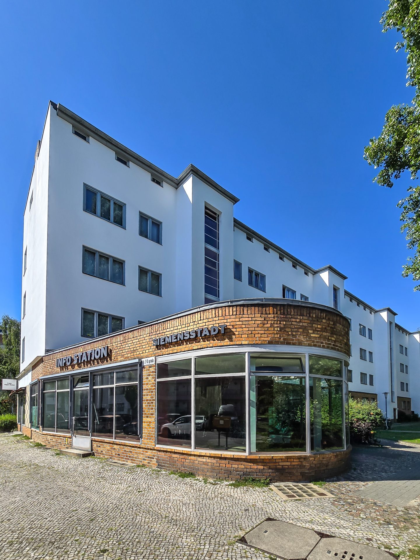 Moderne Architektur: weißes Gebäude mit Glasfront in grünem Umfeld unter blauem Himmel.