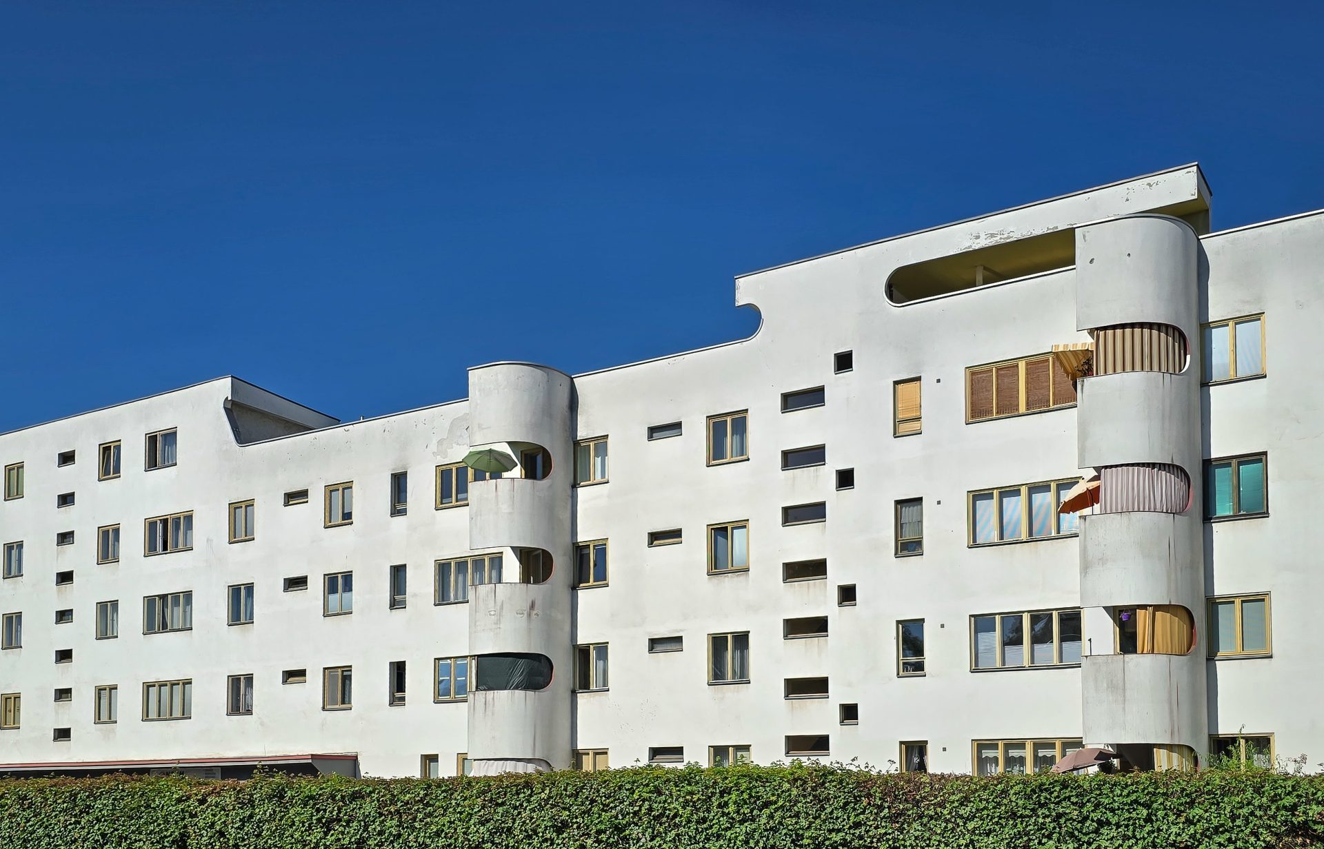 Moderne Wohnhäuser mit geschwungener Fassade und großen Fenstern unter einem blauen Himmel.