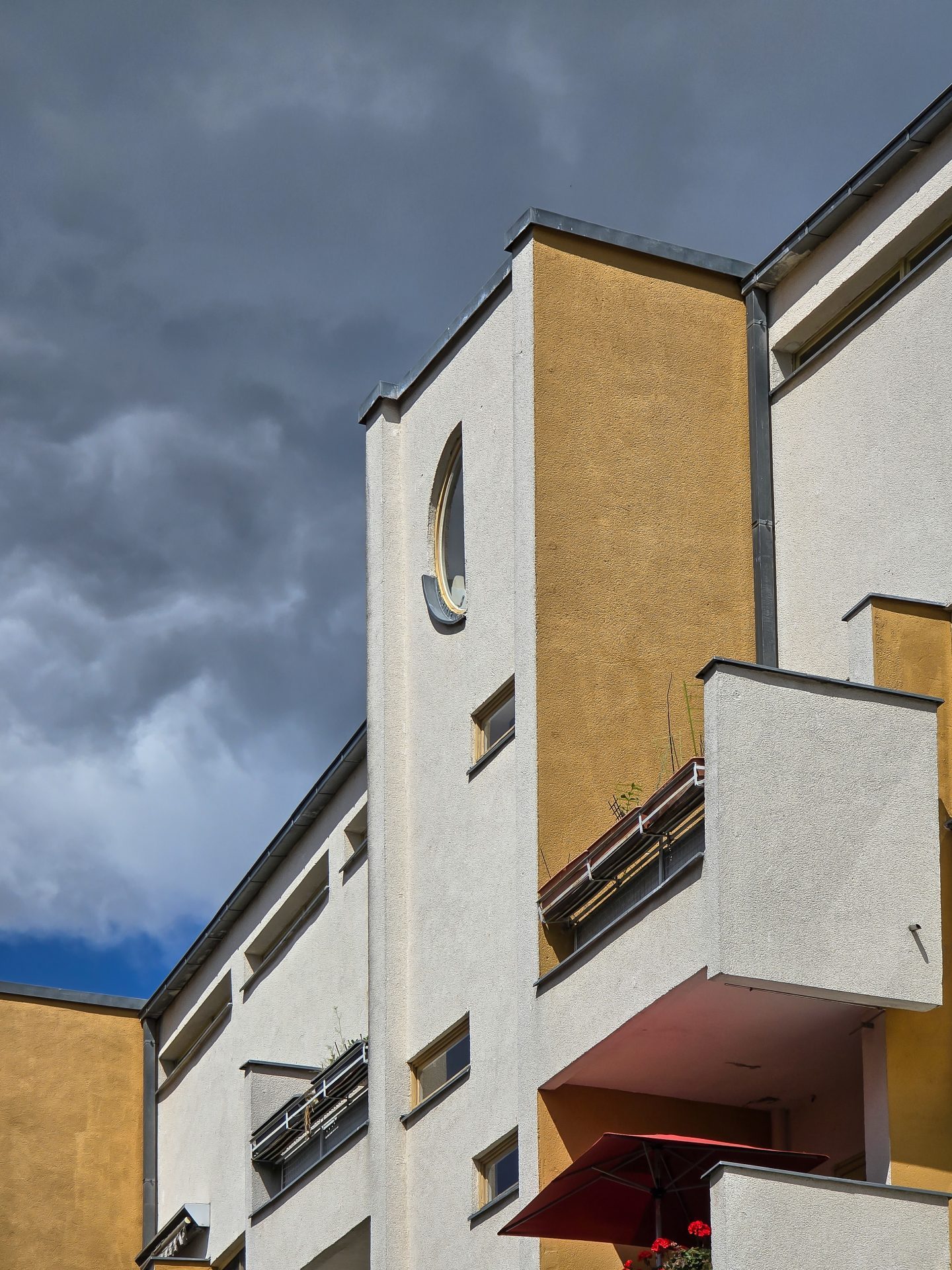 Moderne Architektur mit gelben und weißen Wänden unter einem dramatischen, bewölkten Himmel.