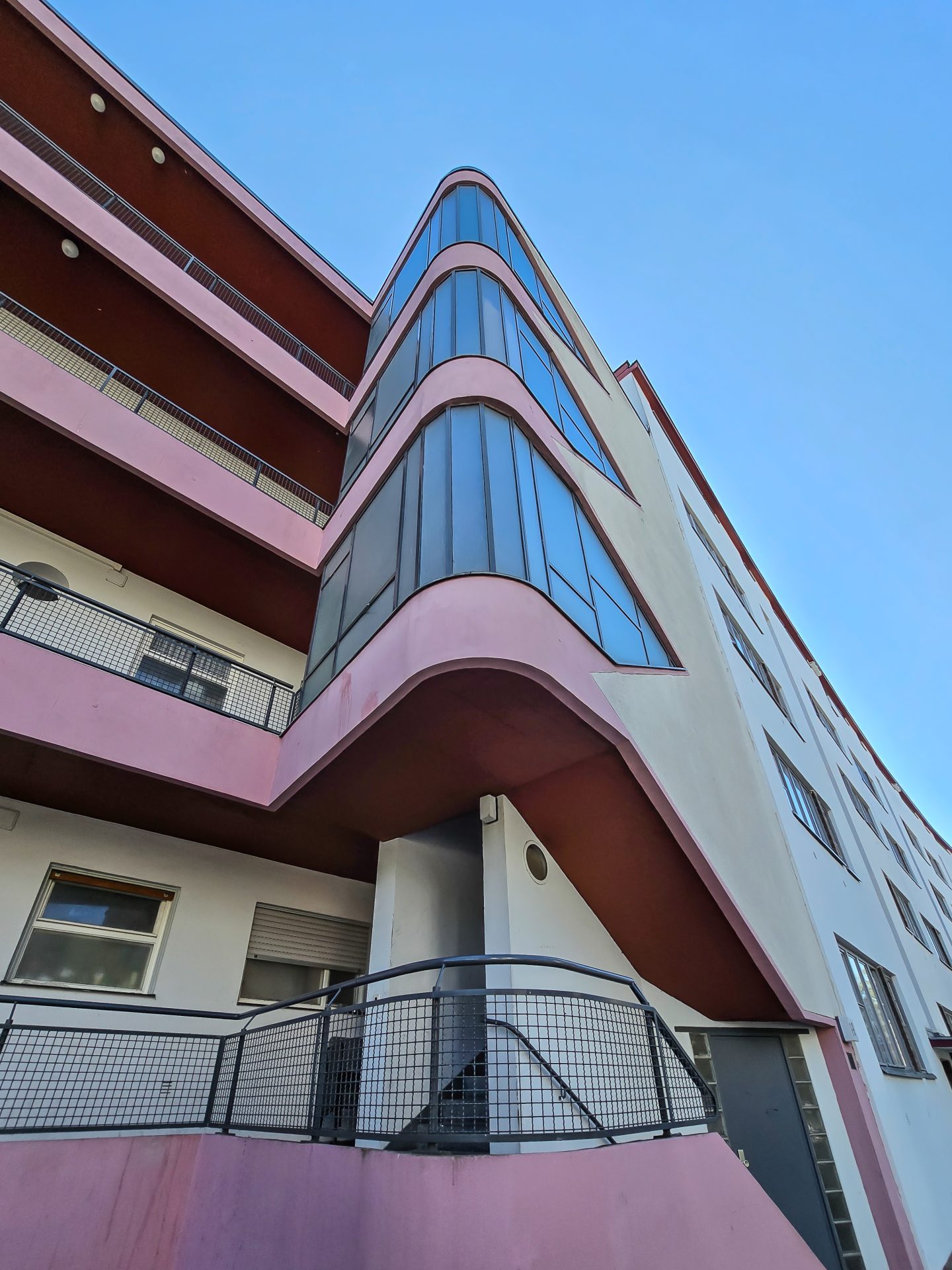 Moderne Gebäudeansicht mit geschwungener Fassade und großen Fenstern, in Pink und Weiß gestaltet.