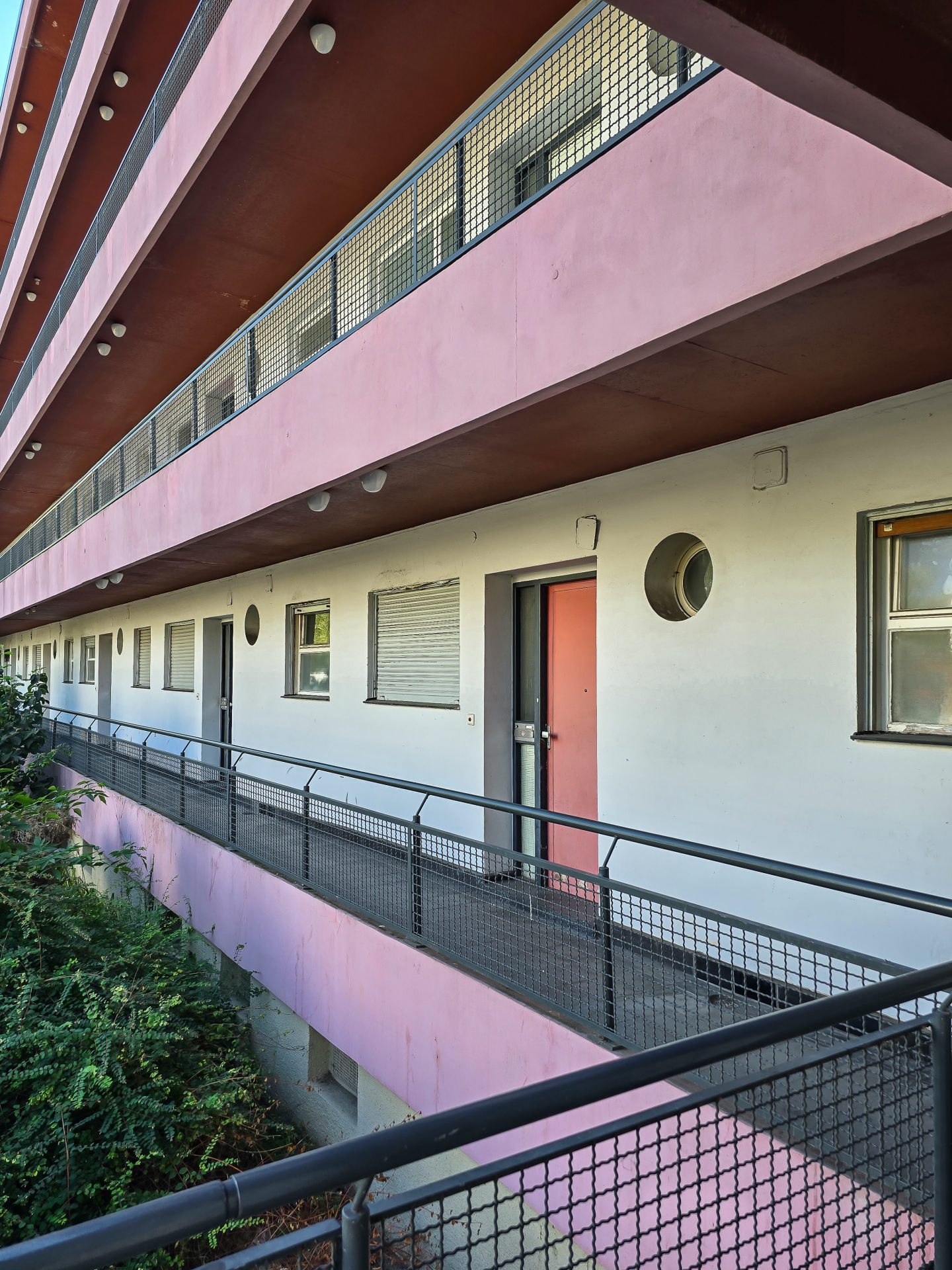 Fassade eines modernen, mehrstöckigen Gebäudes mit pinken Balkonen und klarem, minimalistischen Design.
