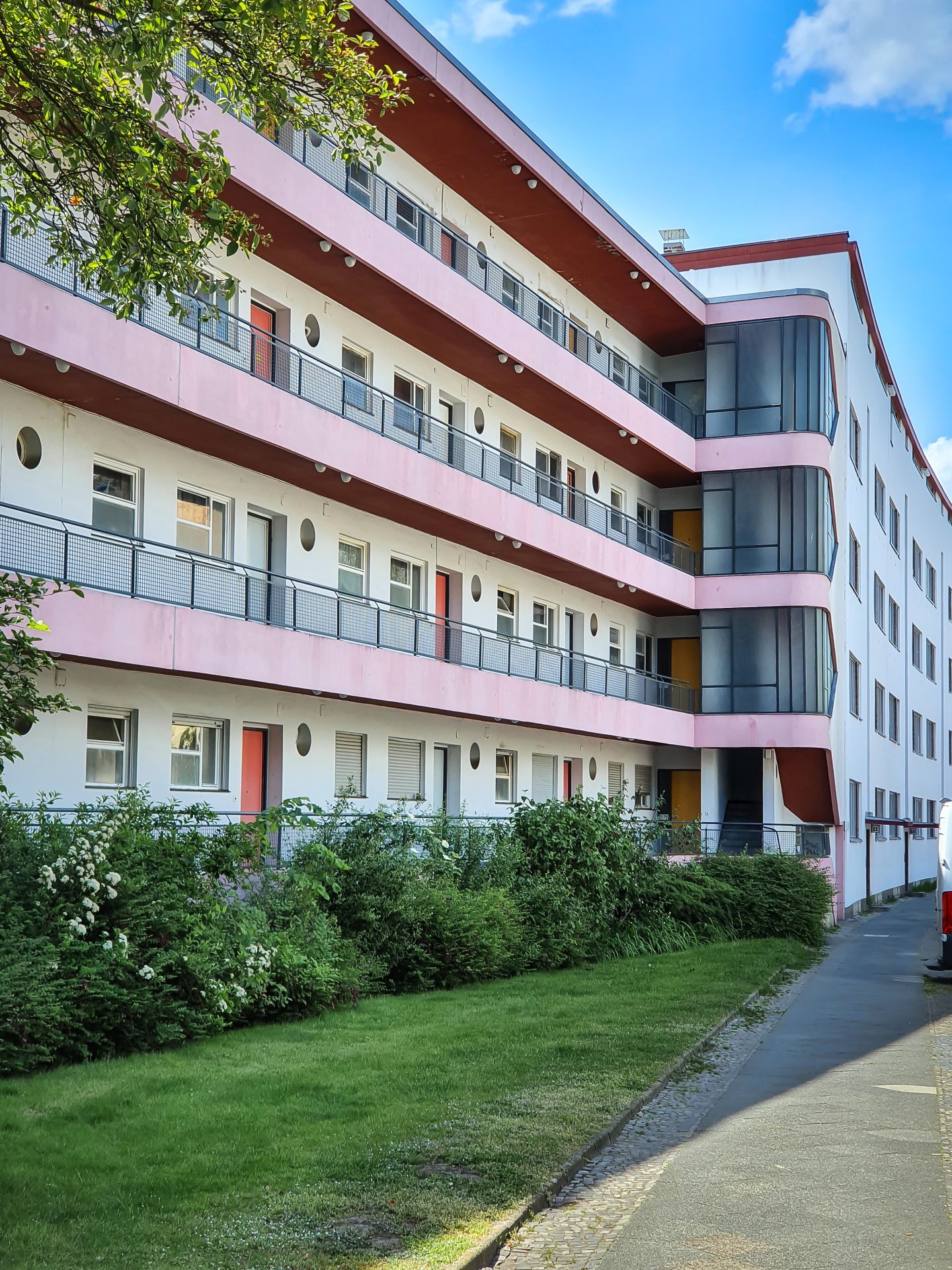 Moderne Wohnanlage mit pinken Designelementen, mehreren Balkonen und umgeben von Rasenflächen und Sträuchern.