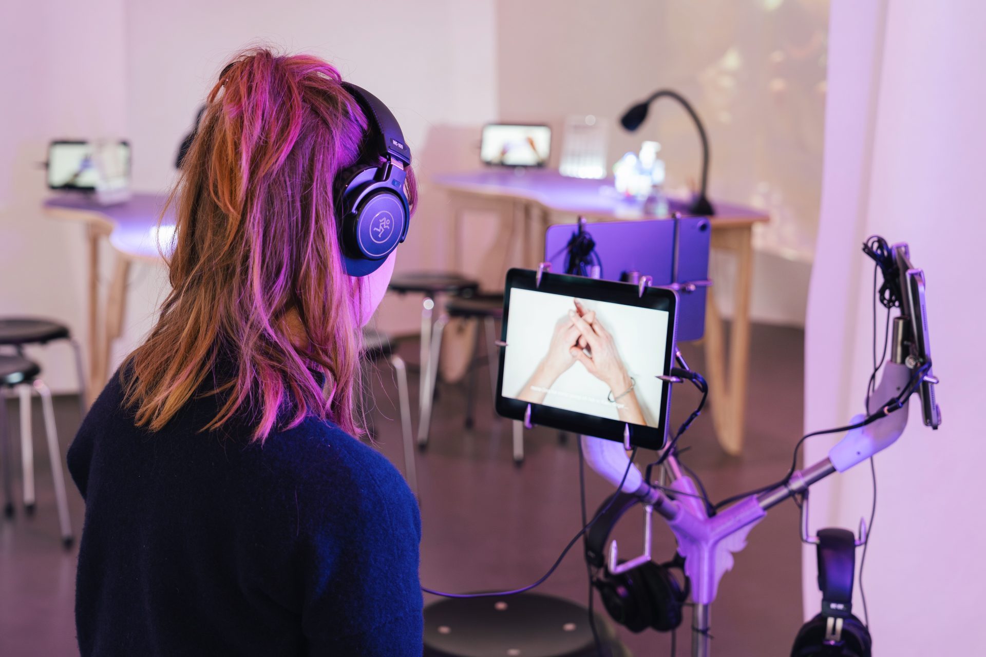 Eine Person mit Kopfhörern schaut sich ein Video auf einem Tablet in einem modernen Ausstellungsraum an.