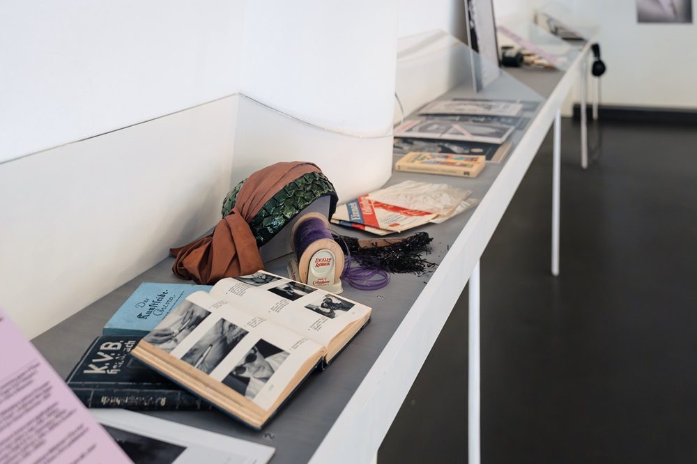 Eine Galerieansicht mit Büchern, Zeitschriften und Gegenständen auf einem Tisch. Kunsthandwerk und Schreibwaren sind zu sehen.