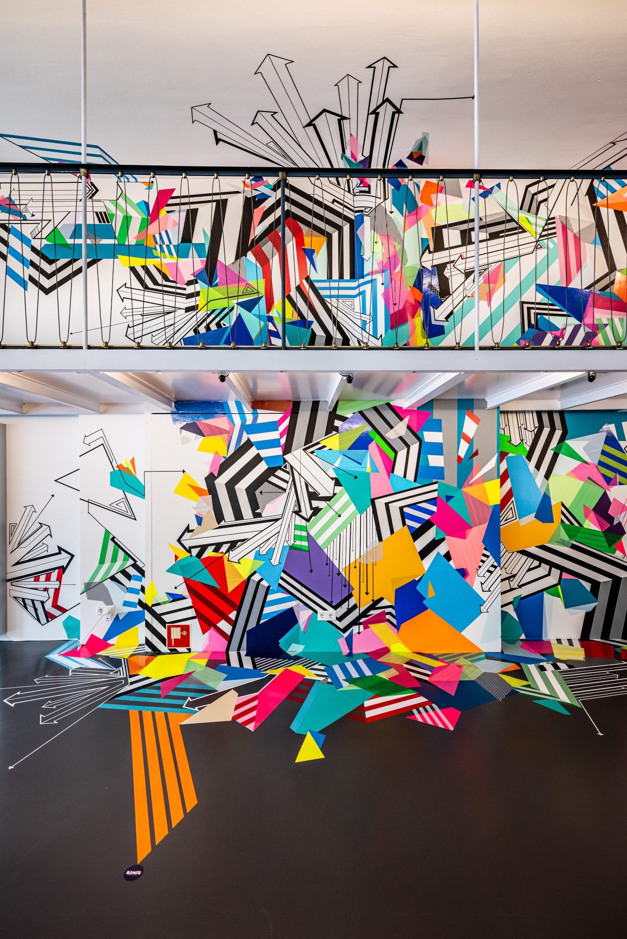 Buntes Wandgemälde mit geometrischen Formen und Linien, das den Raum lebendig und dynamisch wirken lässt.