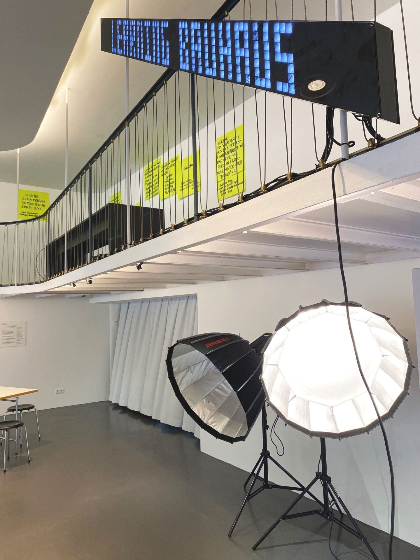 Innenansicht eines modernen Raumes mit großen Scheinwerfern und einer digitalen Anzeige, die "LEARNING BAUHAUS" zeigt.