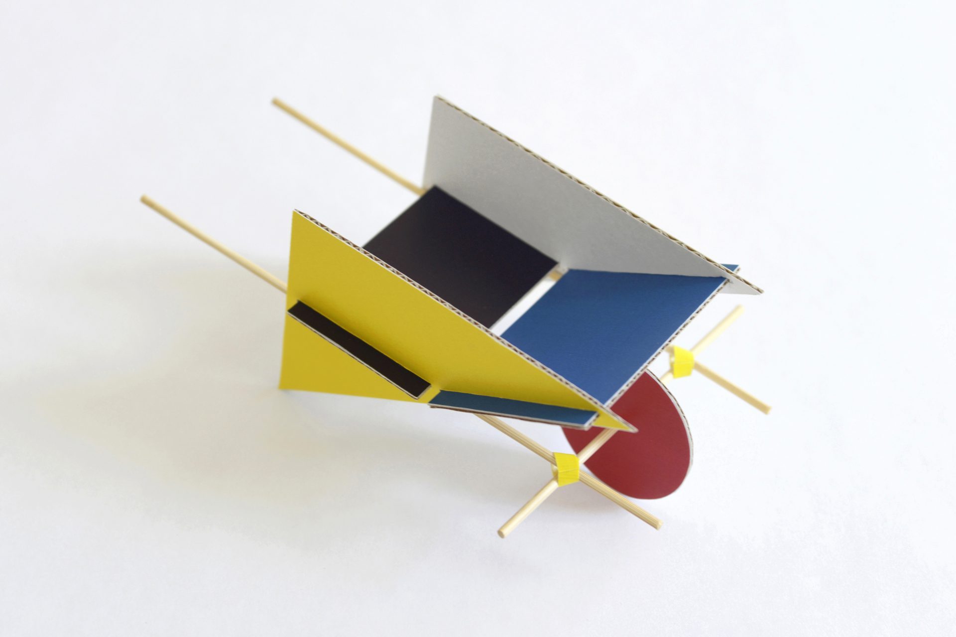 Bunte geometrische Modellkonstruktion aus Karton und Holzstäbchen auf sanftem Hintergrund.