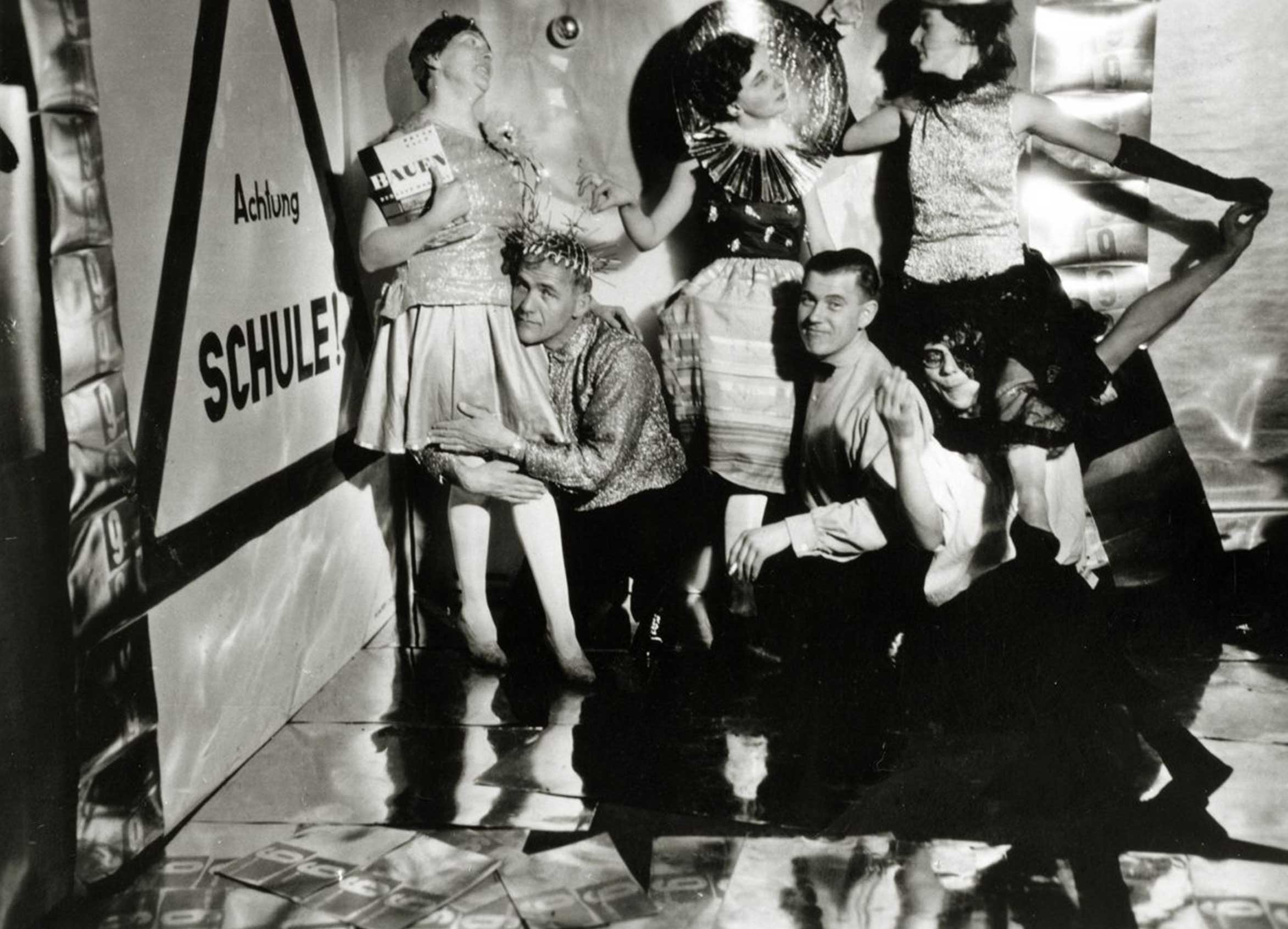 A black-and-white photo of five people in colorful costumes interacting playfully in a whimsical setting.