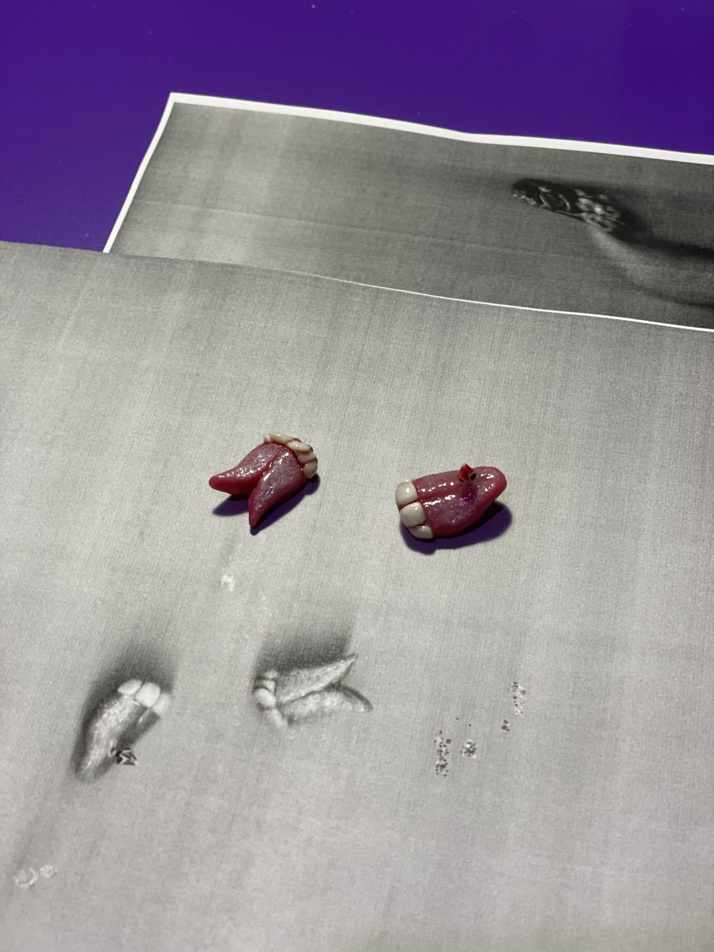 Two red models of teeth are placed on a black-and-white photograph of impressions.