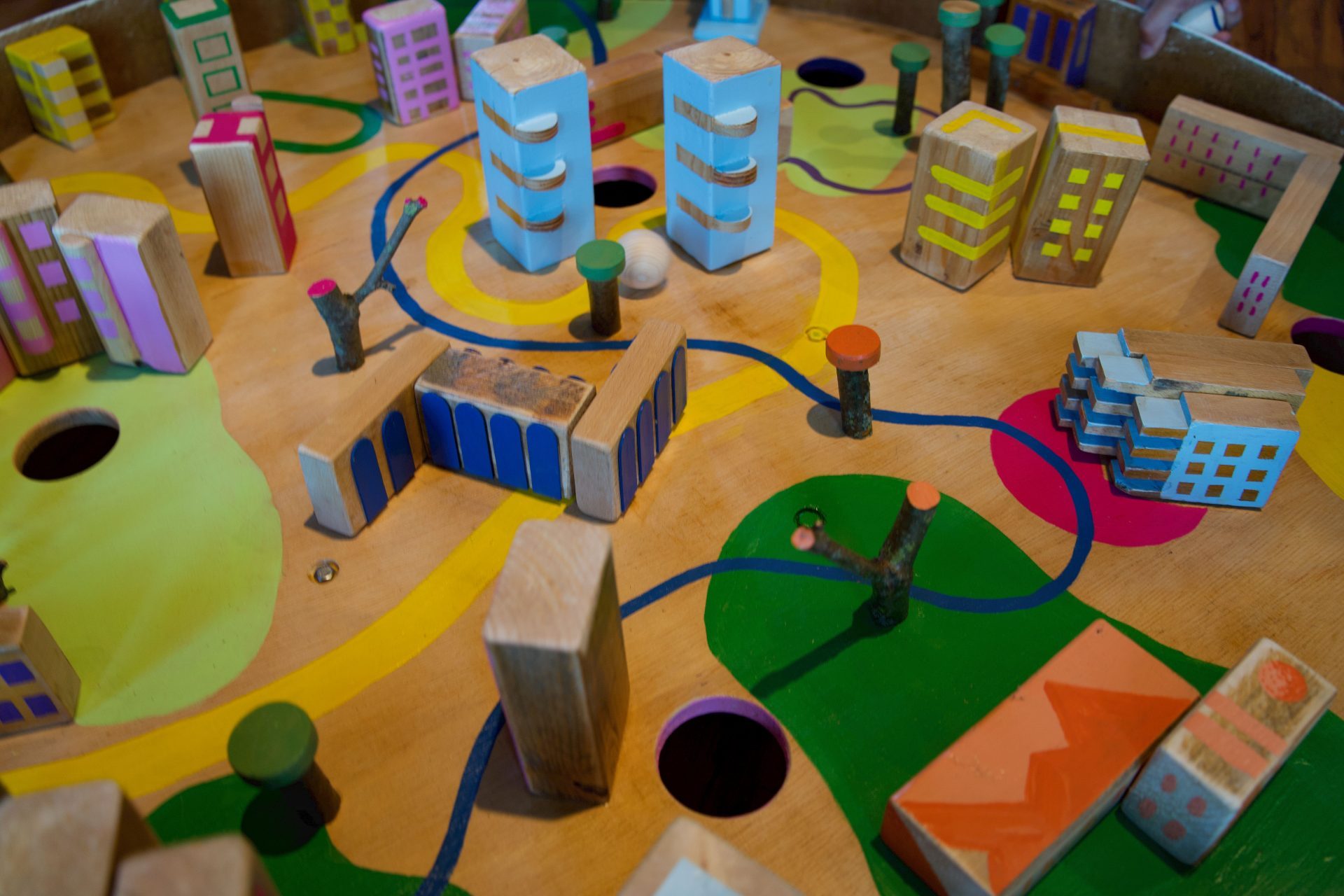 Buntes Holzspielzeug mit einer Miniaturstadt, Gebäuden und Wegen auf einer Spieloberfläche.