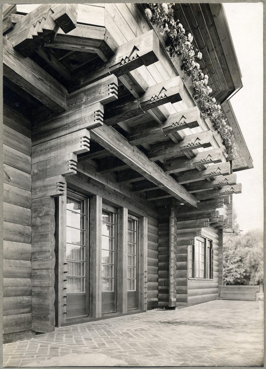 Detailaufnahme einer Holzarchitektur mit geschnitzten Balken und großen Fenstern. Historischer Stil in Schwarz-Weiß.
