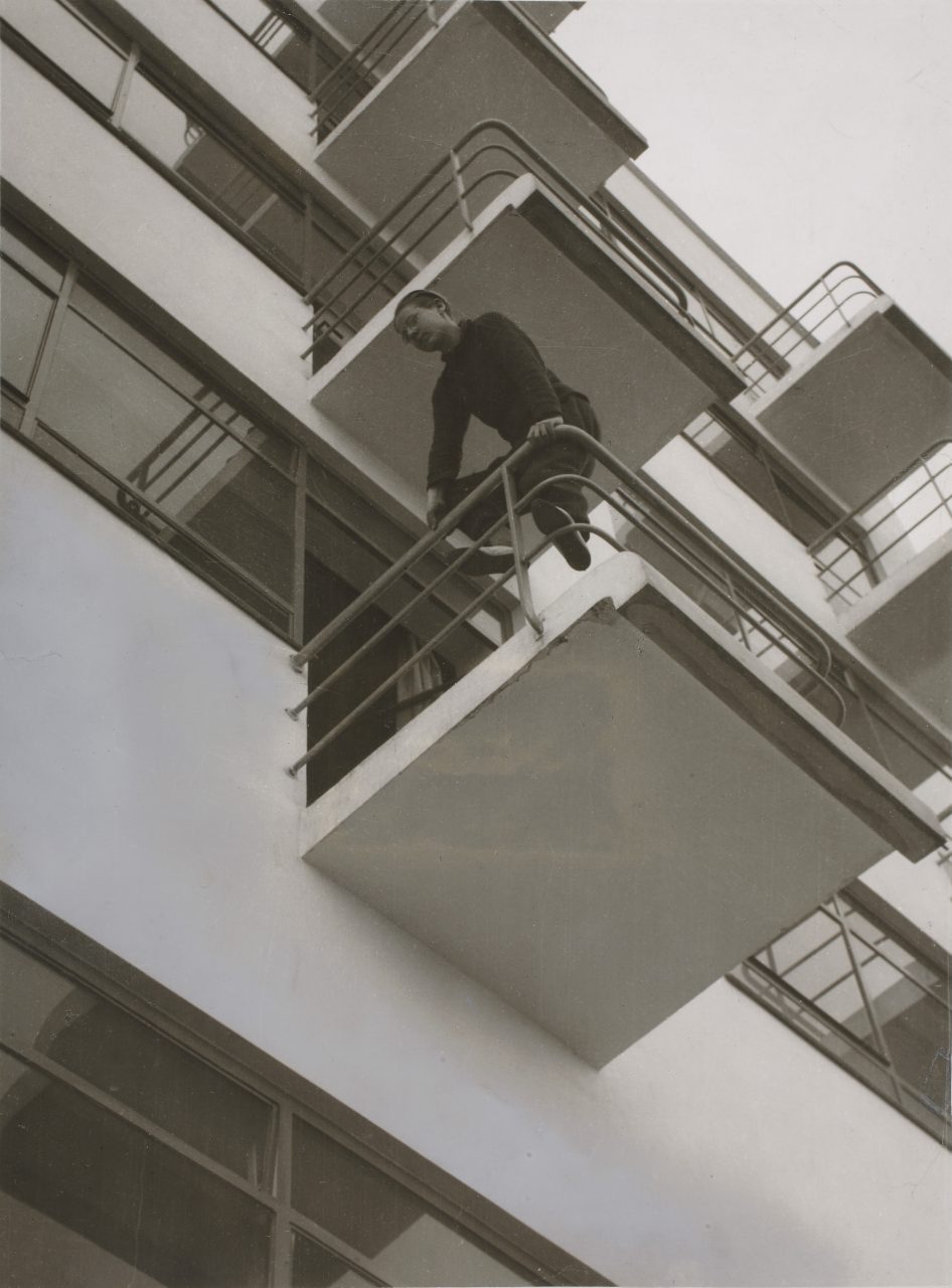 Mann auf einem Balkon lehnt sich über die Brüstung eines modernen Gebäudes. Schwarz-Weiß-Fotografie.