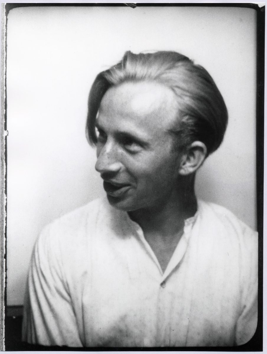 A black and white portrait of a man with light hair, looking to the side, wearing a simple shirt.
