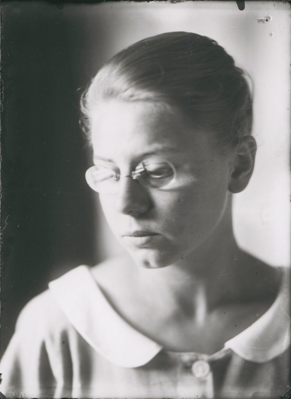 Nachdenkliche Frau mit Brille, die seitlich blickt, in einem sanften Schwarz-Weiß-Porträt.
