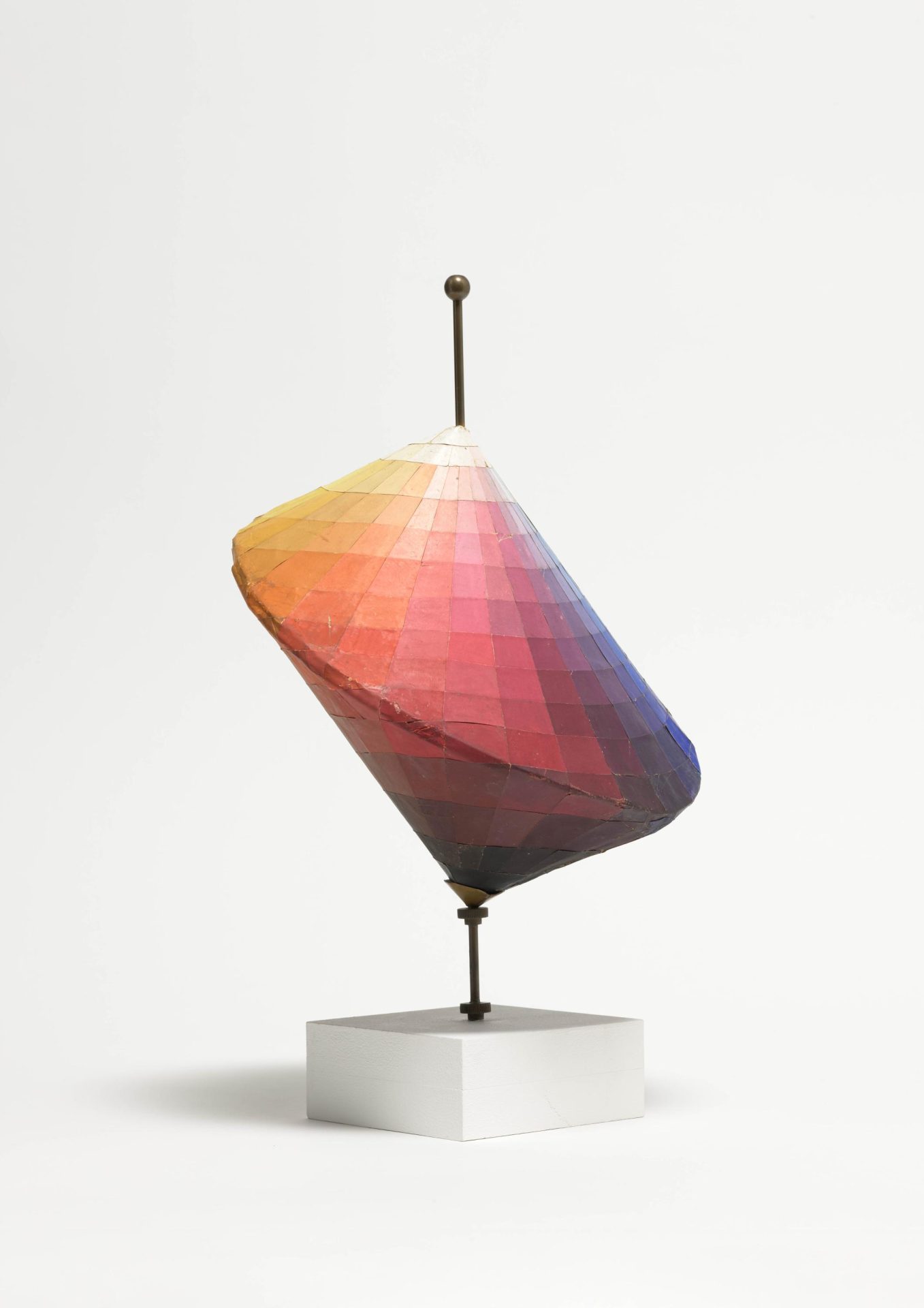 Abstract sculpture in the shape of a cone with colorful geometric surfaces on a white base.