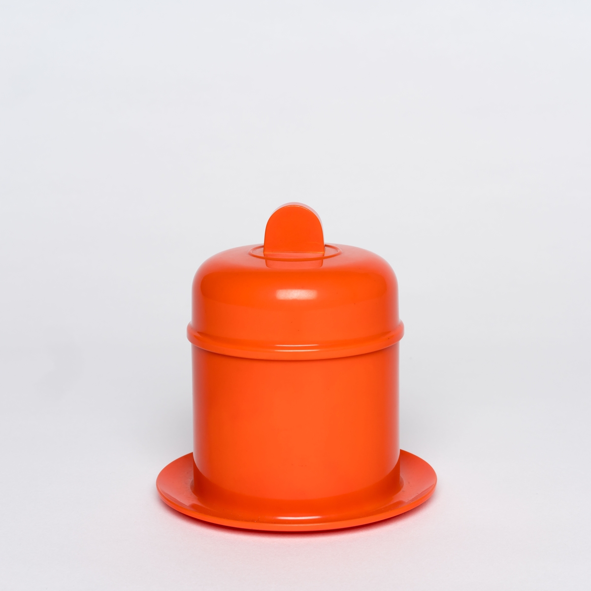 Orangefarbene, runde Dose mit Deckel auf passendem Untersetzer vor neutralem Hintergrund.