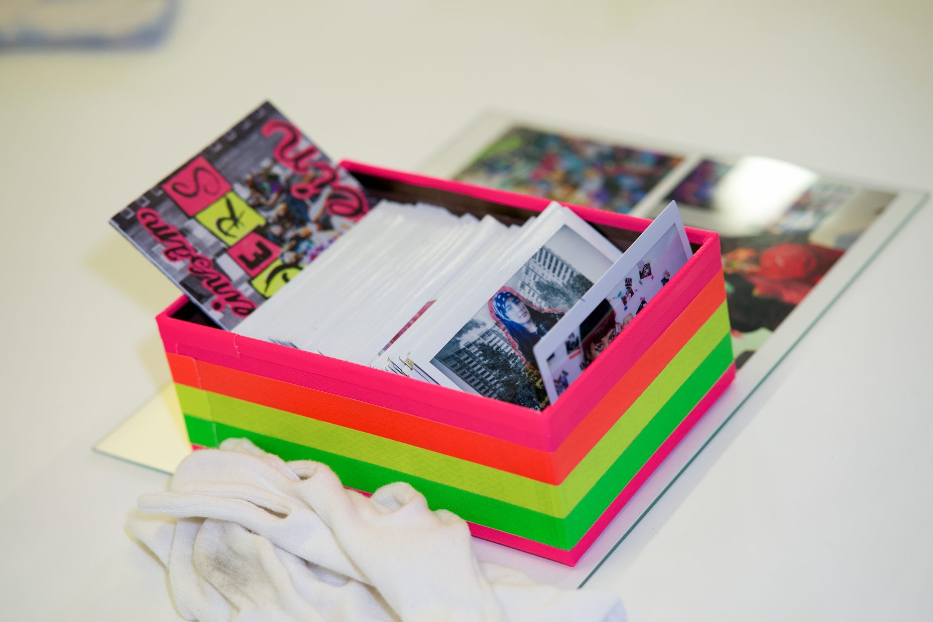 Colorful box with photos and magazines, next to a white cloth and additional pictures on a table.