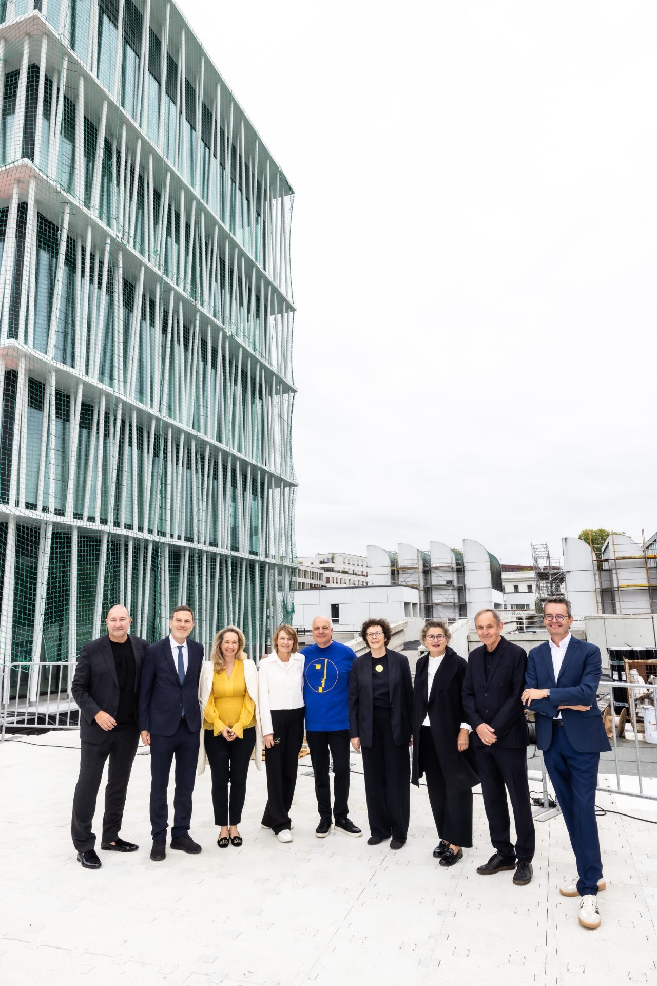 Gruppenszene mit mehreren Personen vor einem modernen Gebäude unter einem bewölkten Himmel.