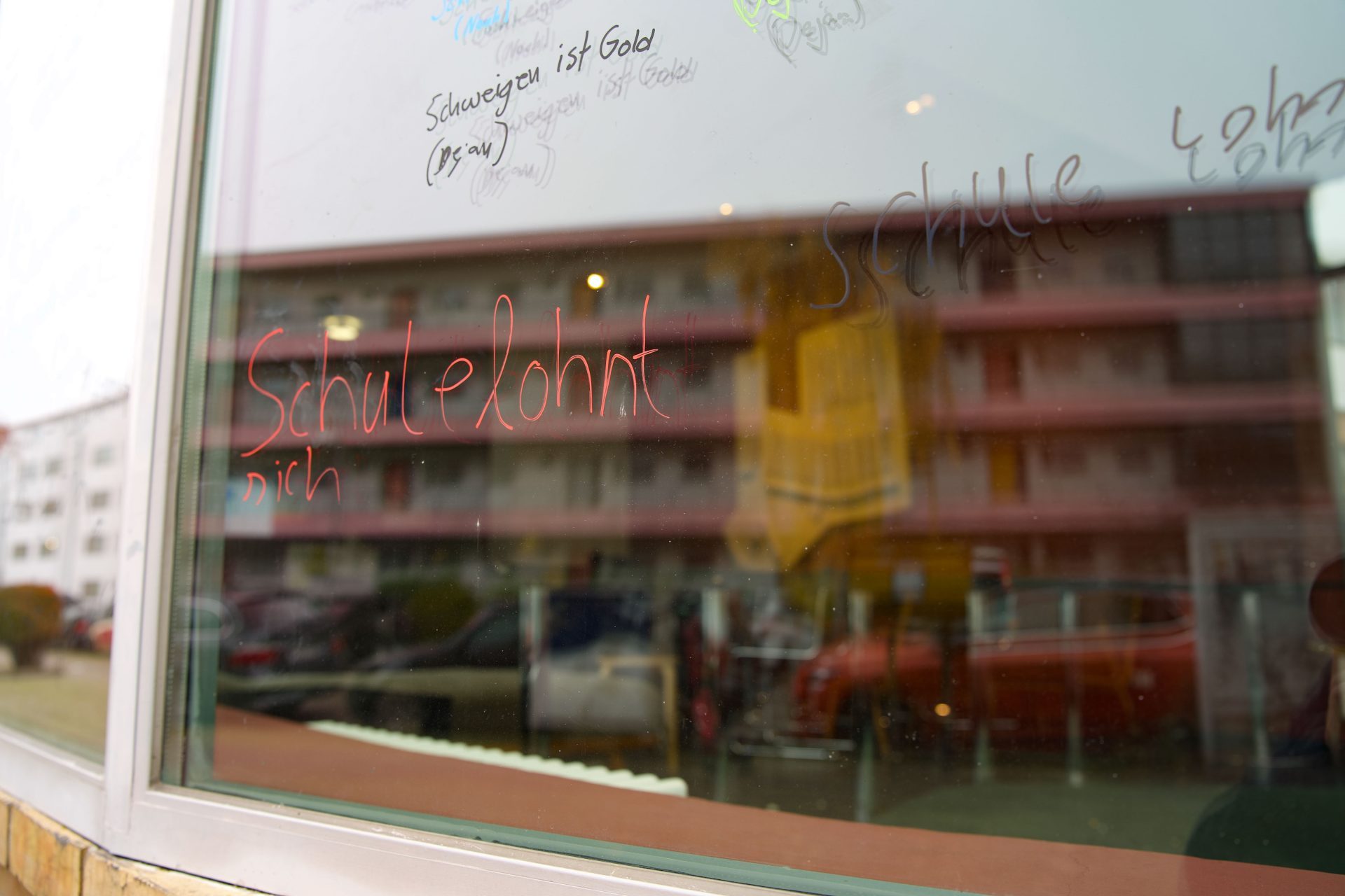 Graffiti auf einem Fensterglas mit der Aufschrift "Schule lohnt sich" und bunten Kritzeleien.