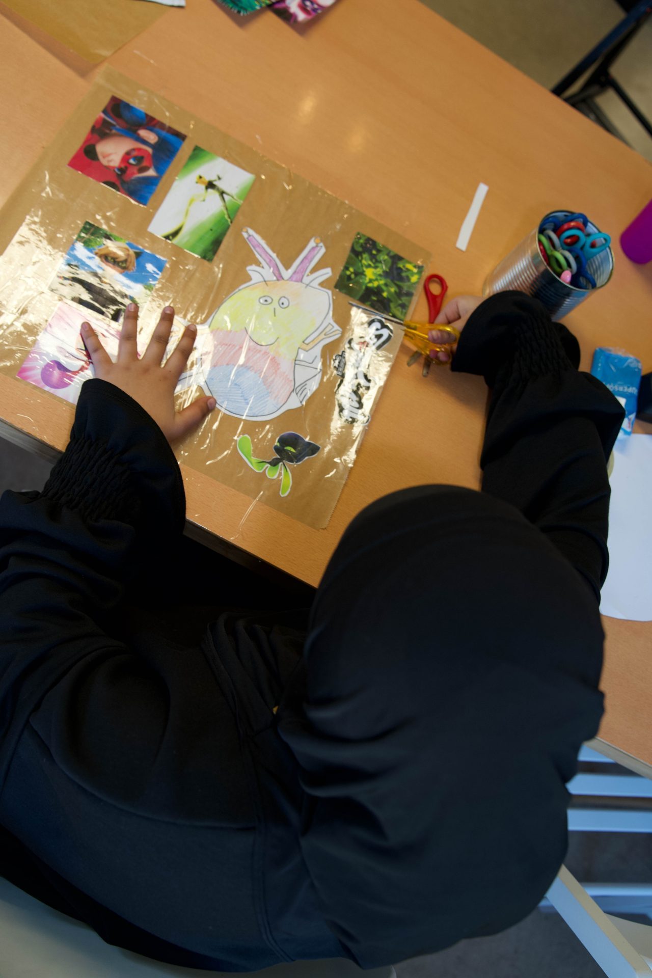 Ein Kind bastelt begeistert mit Bildern und Scheren an einem Projekt auf dem Tisch.