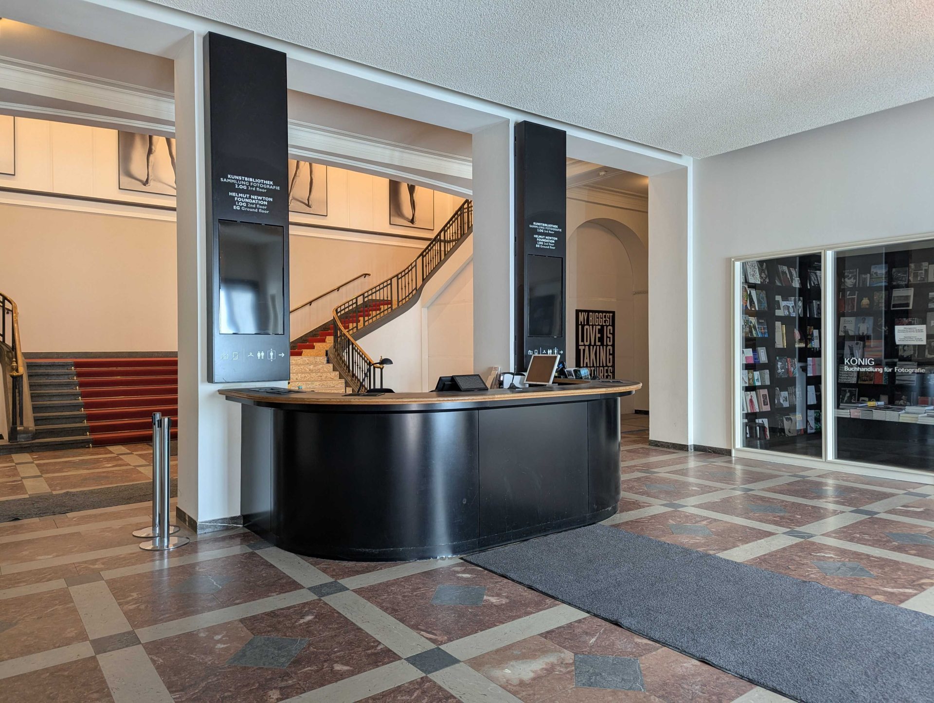 Moderner Empfangsbereich mit schwarzem Empfangstresen, Kunstwerken an der Wand und einer Treppe im Hintergrund.